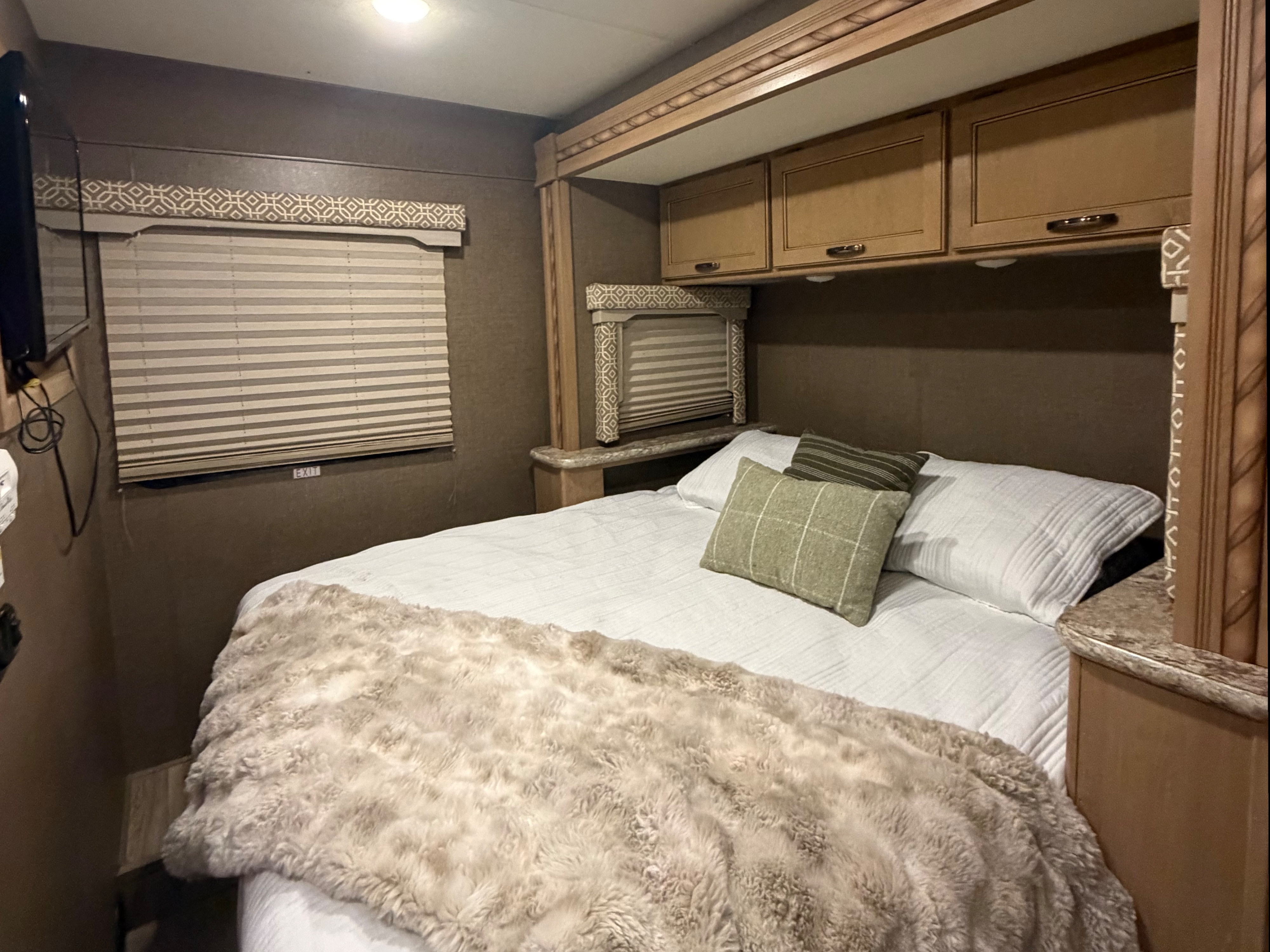 This RV rental bedroom offers a cozy bed with a furry throw, overhead cabinets, and window blinds for a relaxing stay.. Thor Freedom Elite 2017