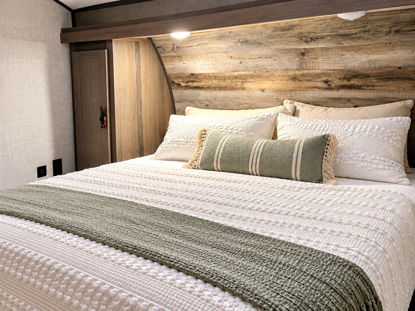 This cozy RV rental bedroom features a rustic wooden headboard, soft white bedding, and a sage green throw, creating a welcoming space.. Gulf Stream Conquest 2022