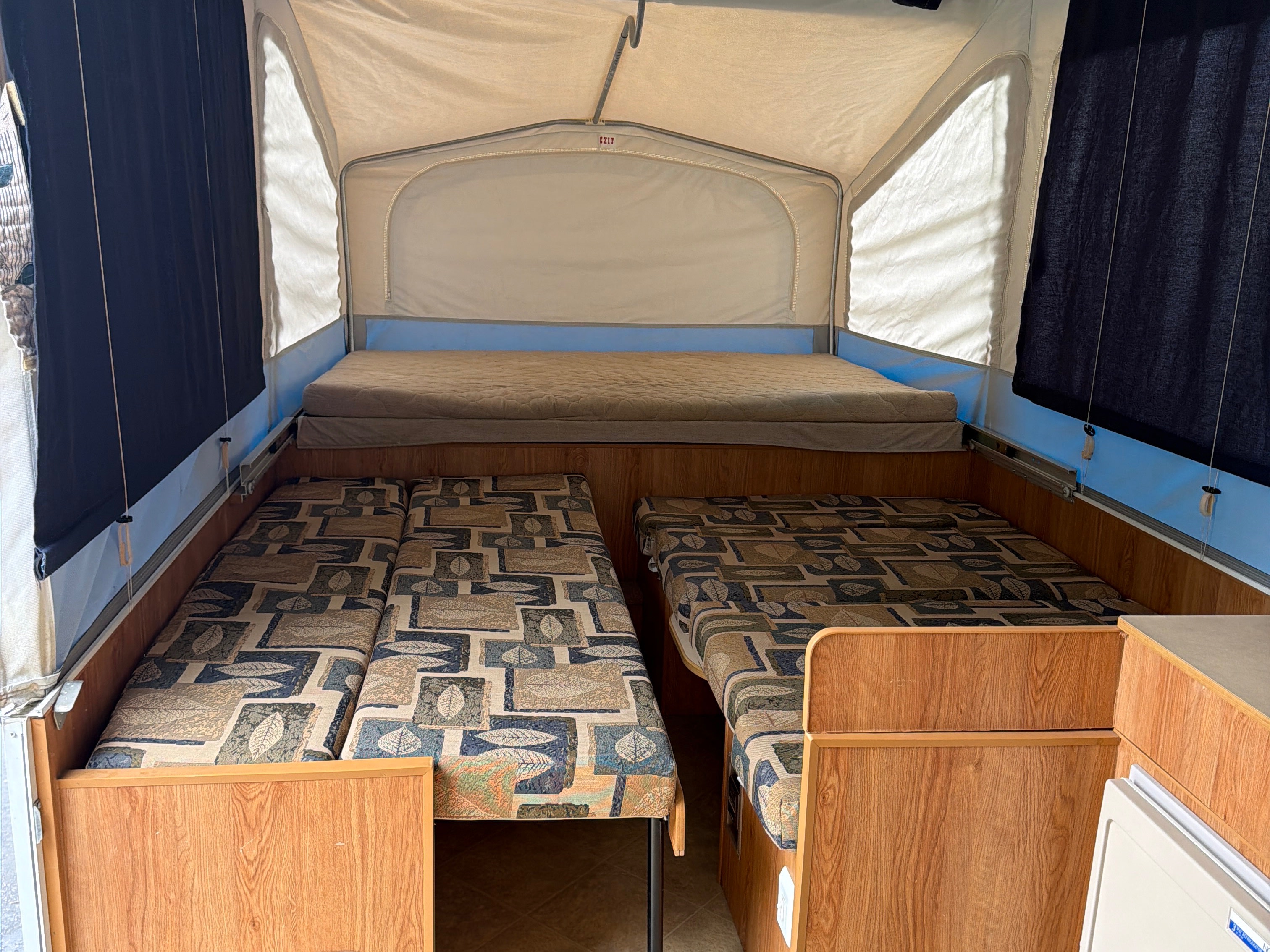Pop-up camper interior of an rv rental, featuring an elevated bed, two lower beds, and wood accents.. Jayco Jay 2009