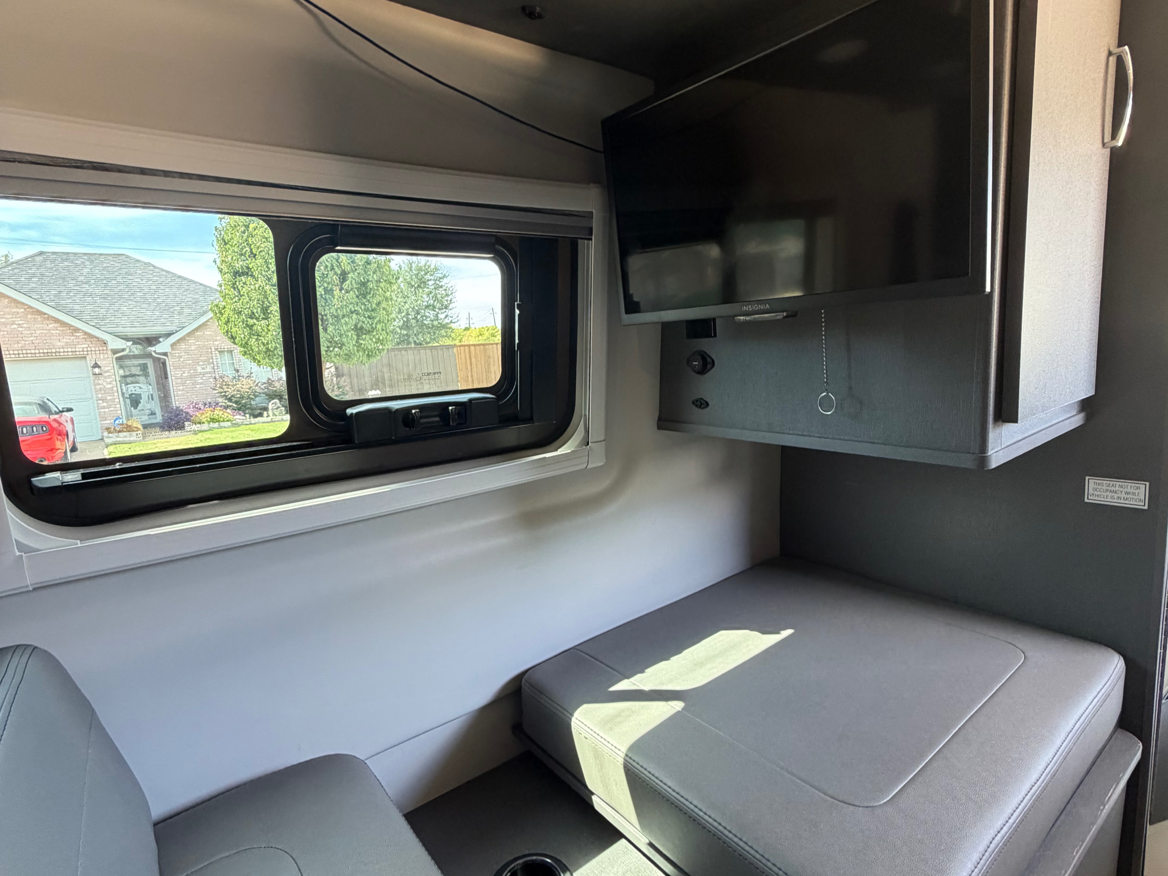 View inside an rv rental: mounted TV, window with outdoor scenery, and gray cushioned seating.. Thor Tranquility 2025