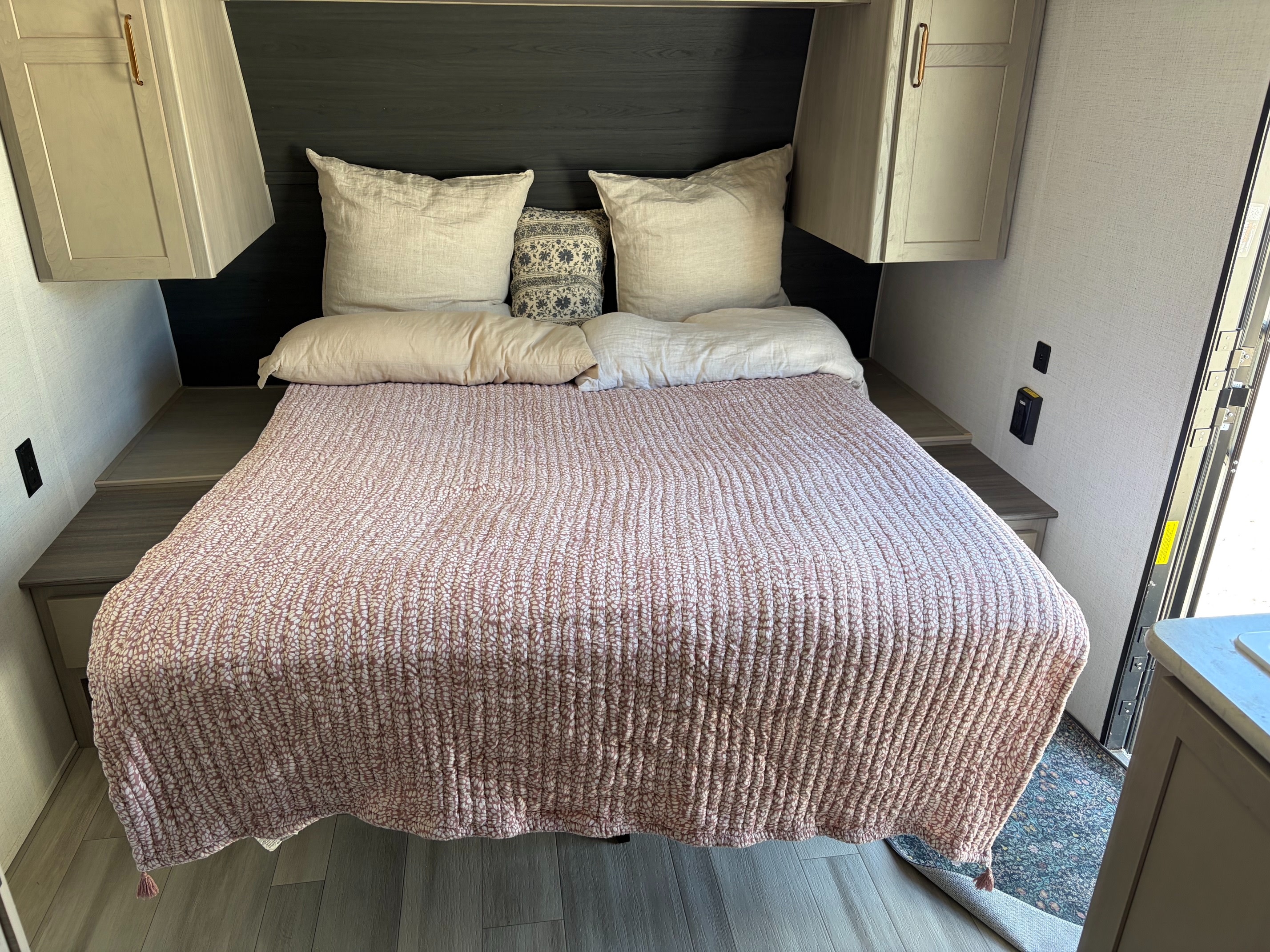 Inviting RV rental bedroom with a comfy bed, neutral pillows, a pink patterned quilt, and convenient overhead cabinets.. Keystone RV Springdale 2024