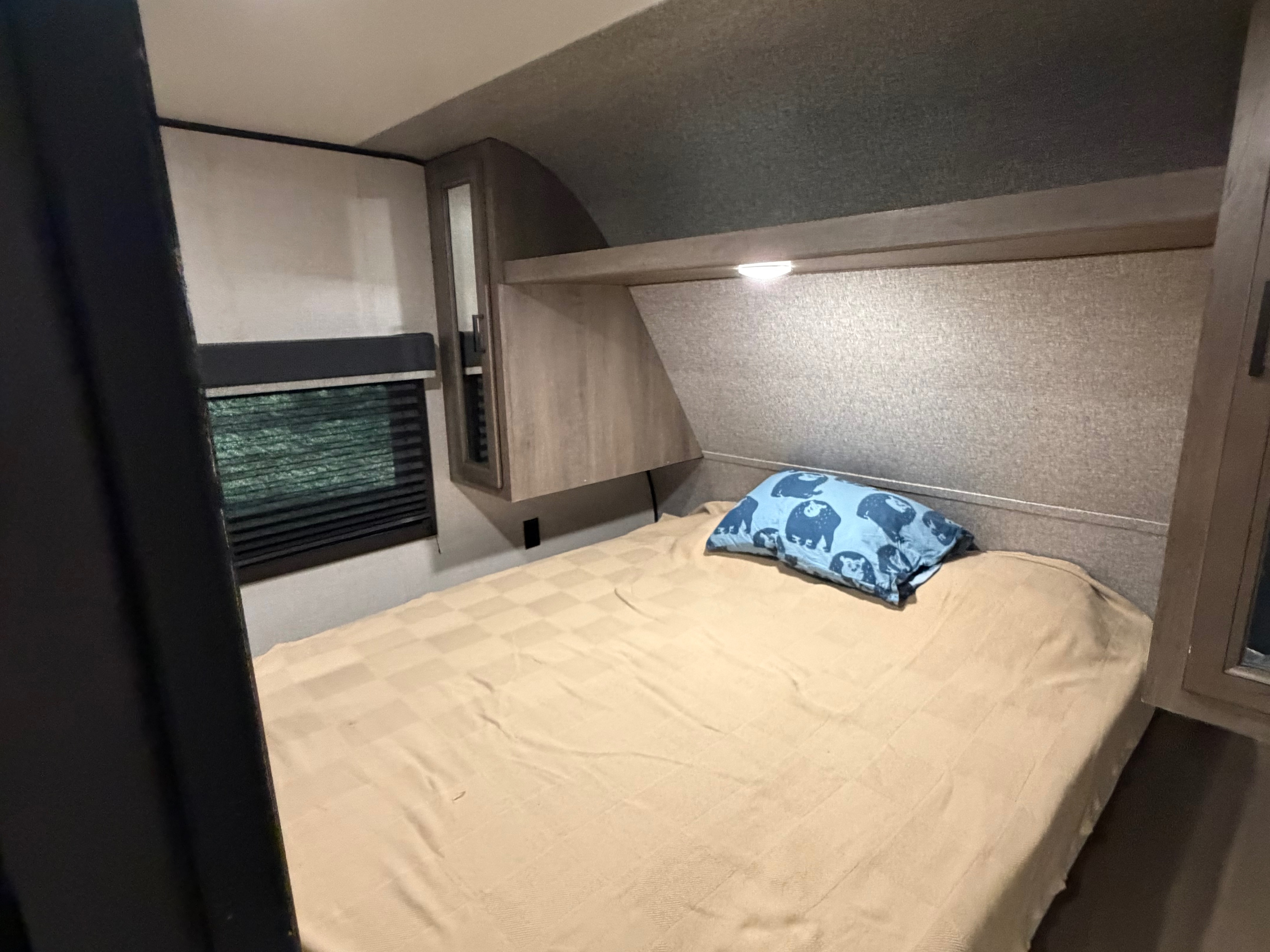 Cozy RV rental bedroom with a compact bed, blue bear pillow, window, and convenient overhead storage.. Starcraft Autumn Ridge 2022