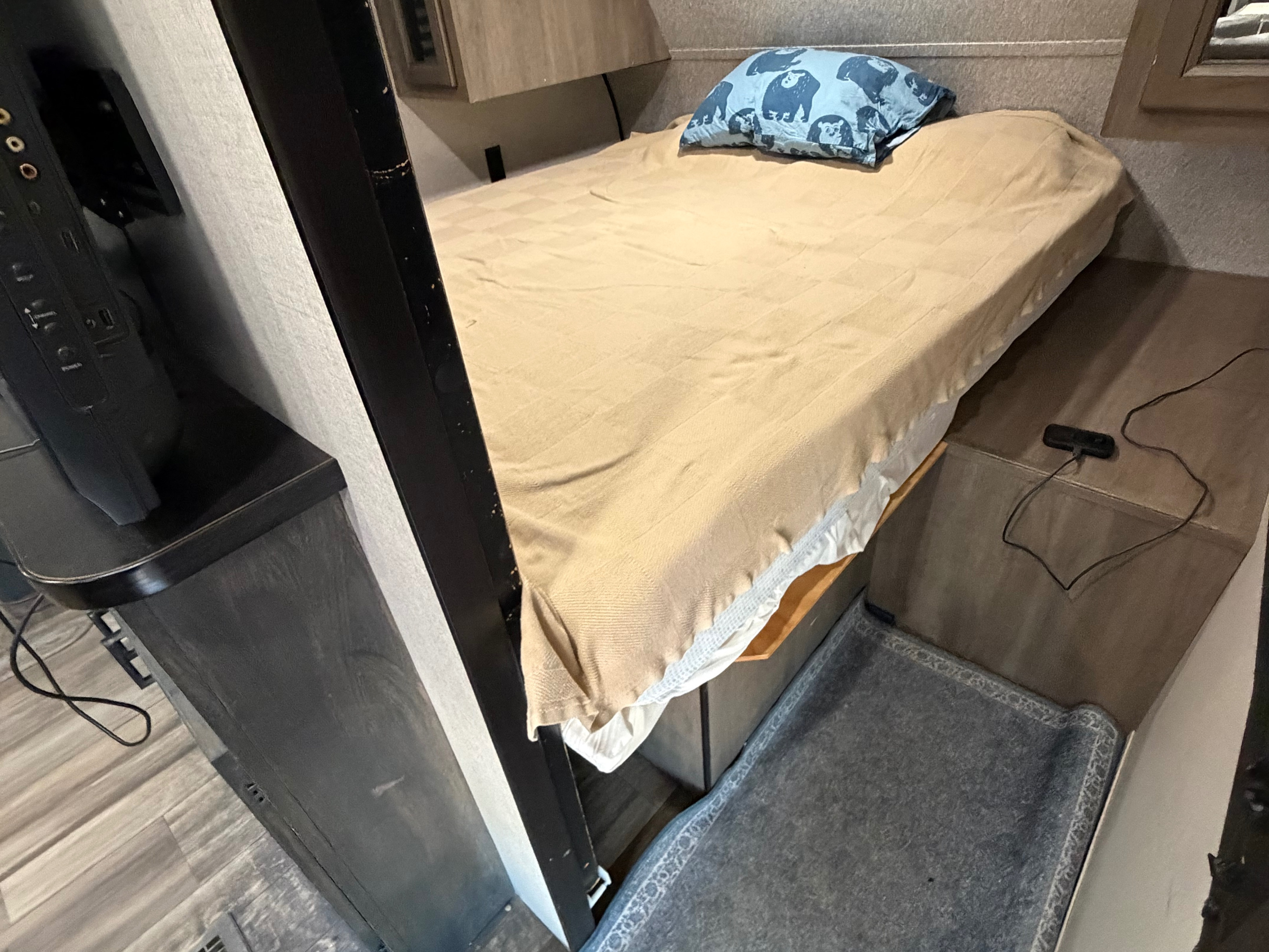 Cozy RV rental bunk bed area featuring a bed with a bear-patterned pillow, a TV stand, and a gray pet bed below.. Starcraft Autumn Ridge 2022