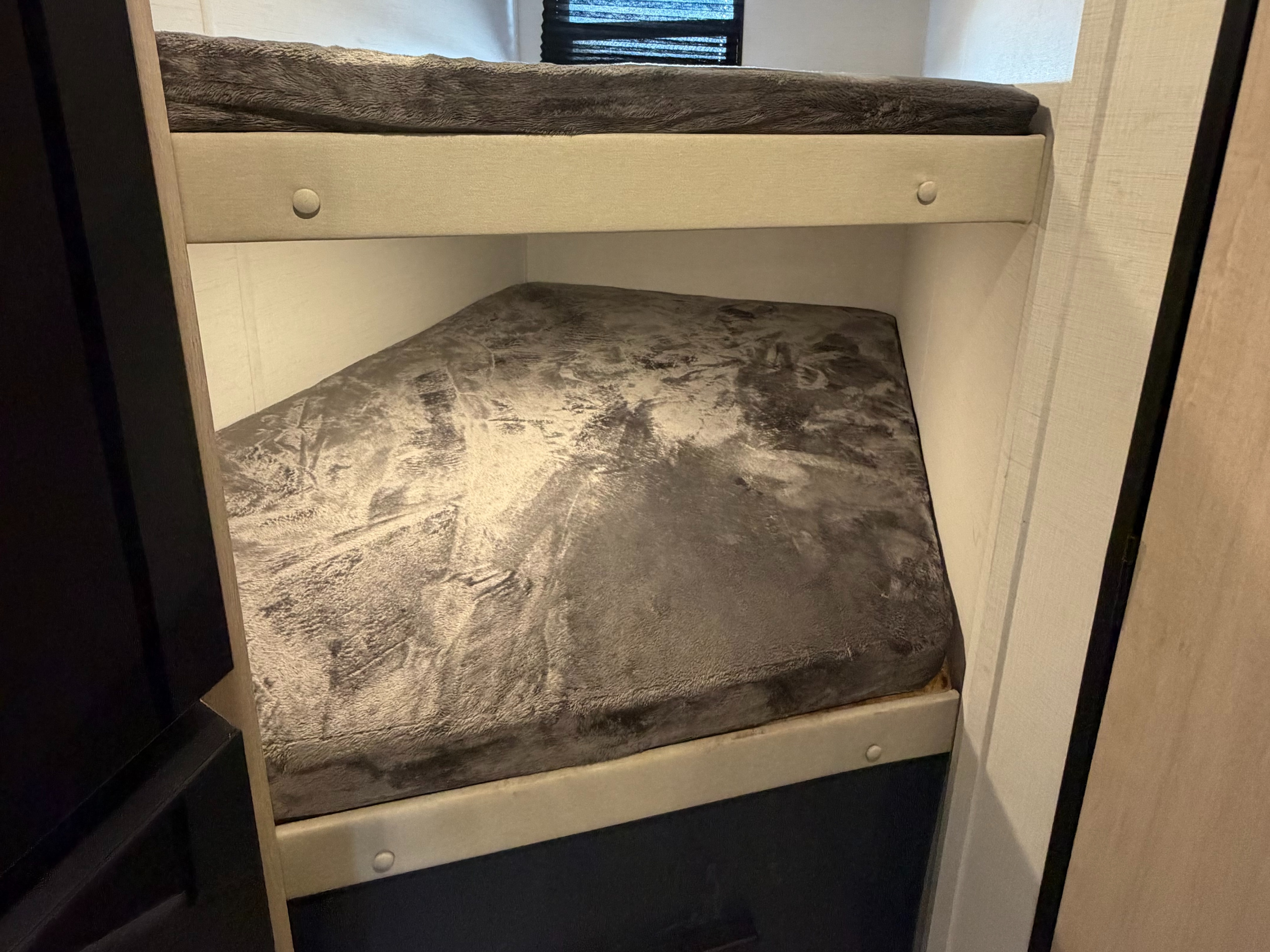 Compact bunk beds in an RV rental, featuring grey textured bedding on both upper and lower bunks, offering a cozy sleeping space.. Avenger Avenger Trailer 2026
