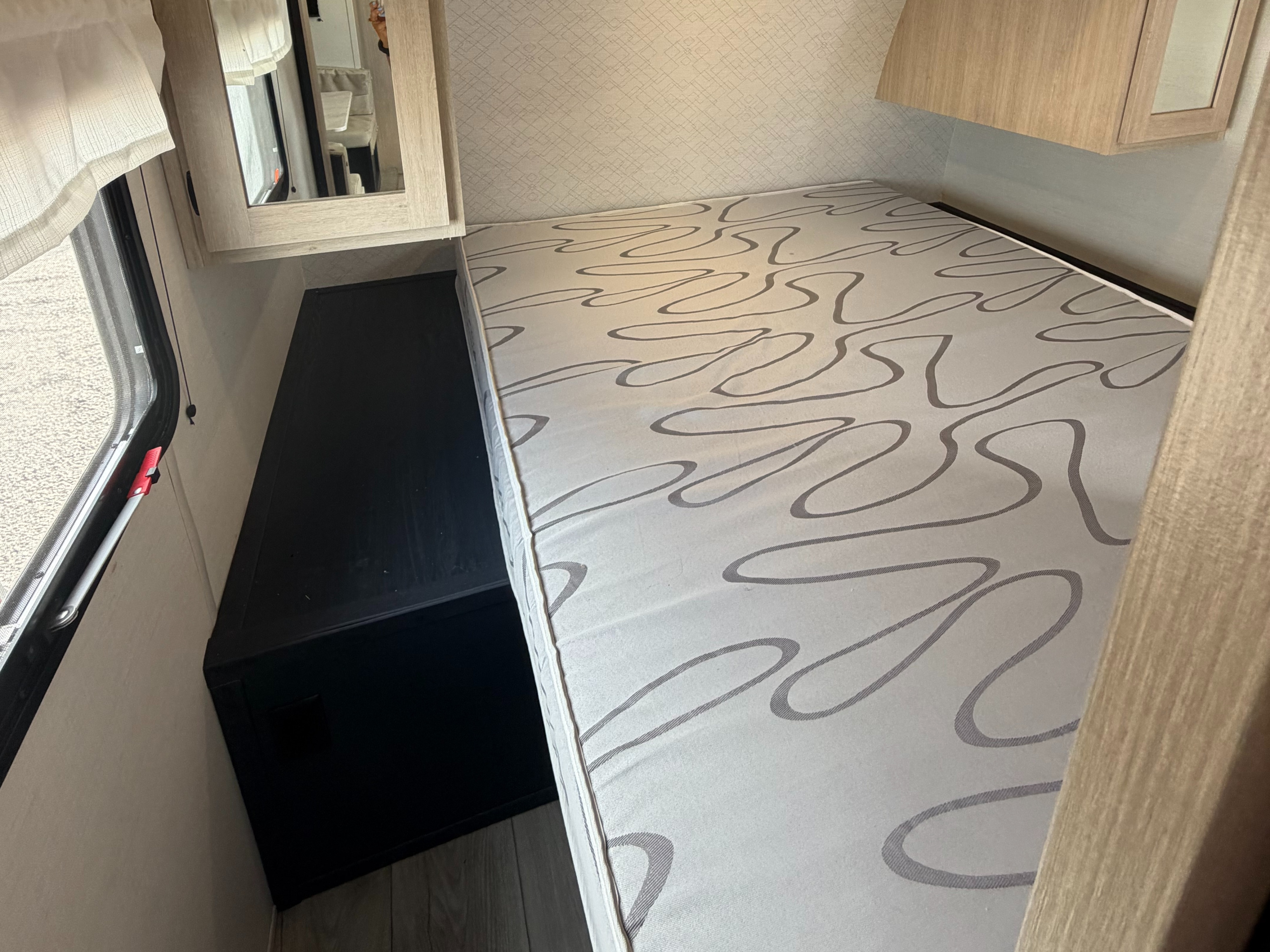 Cozy RV rental interior: bed with patterned mattress, dark storage unit, mirrored cabinet, and window with a curtain.. Avenger Avenger Trailer 2026