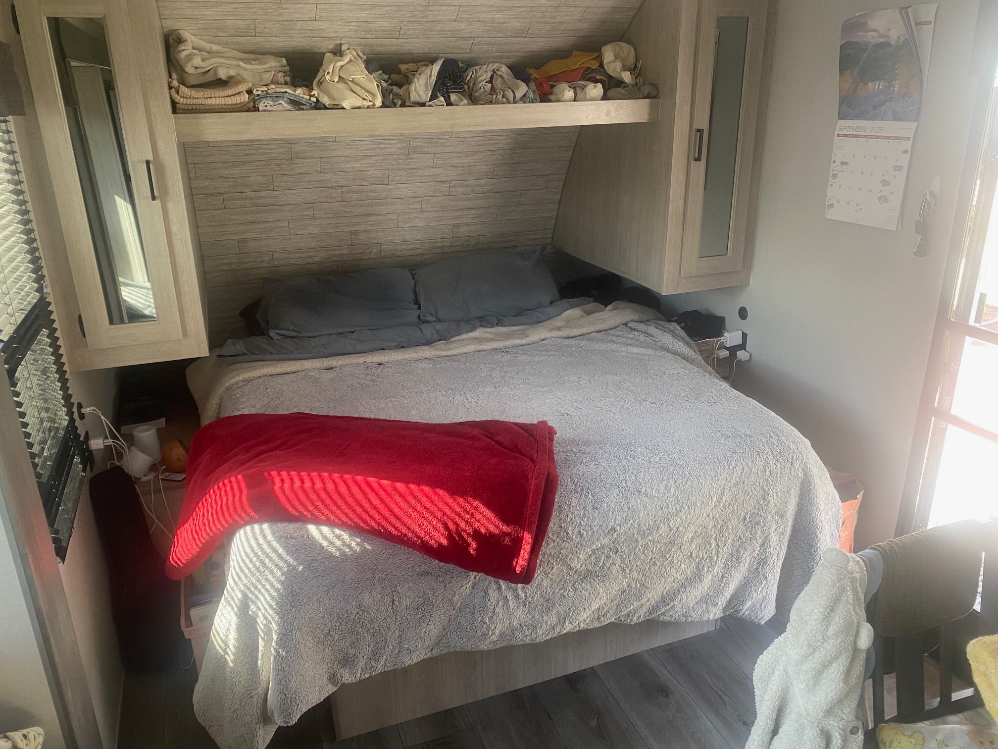 Cozy RV rental bedroom with a comfy bed, overhead storage, and a sunlit window creating striped shadows.. Coachmen Catalina Summit 2024
