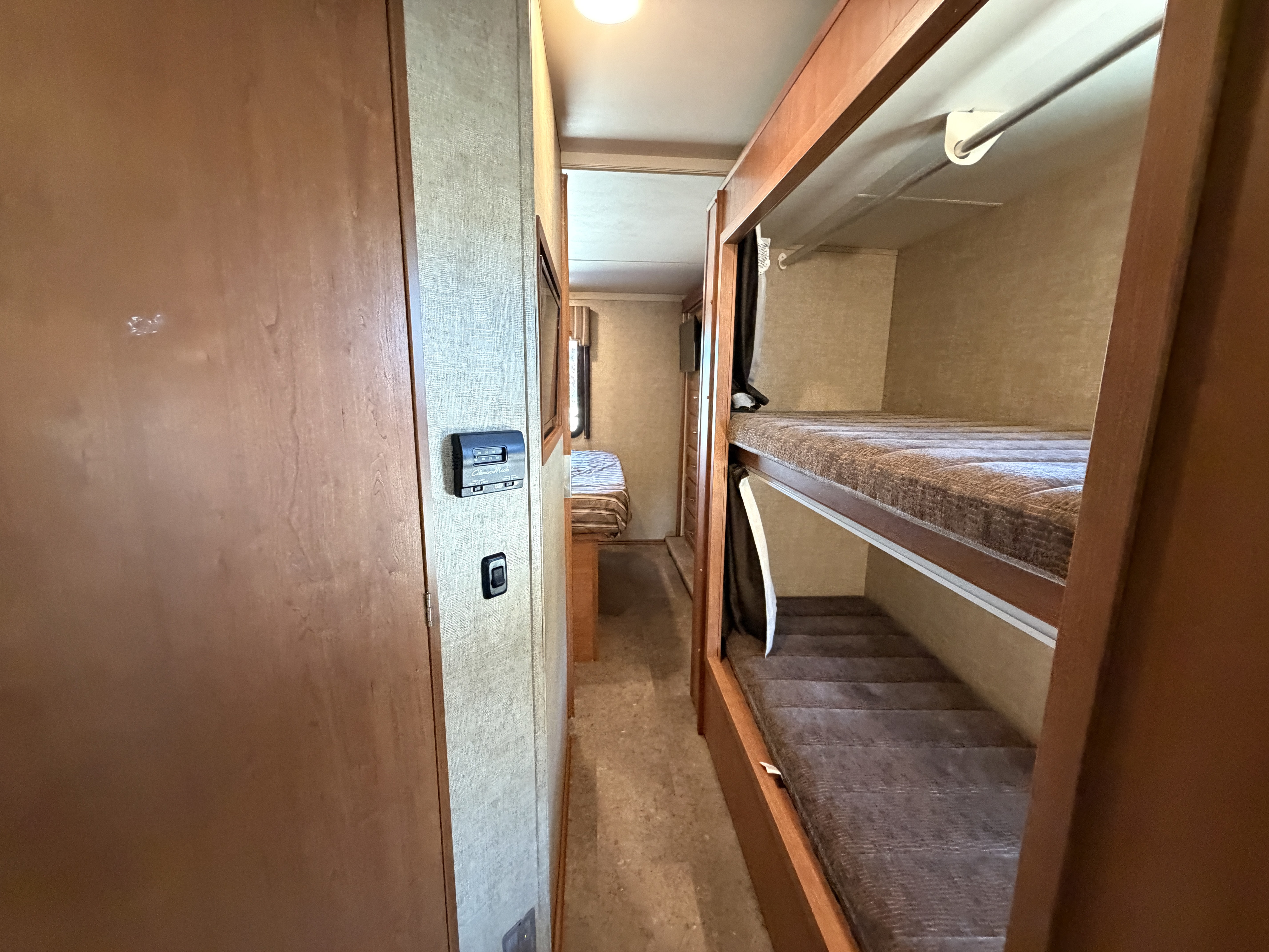 Inside an RV rental: a hallway view with built-in bunk beds on the right and a wall-mounted thermostat visible.. Winnebago Minnie Winnie 2017
