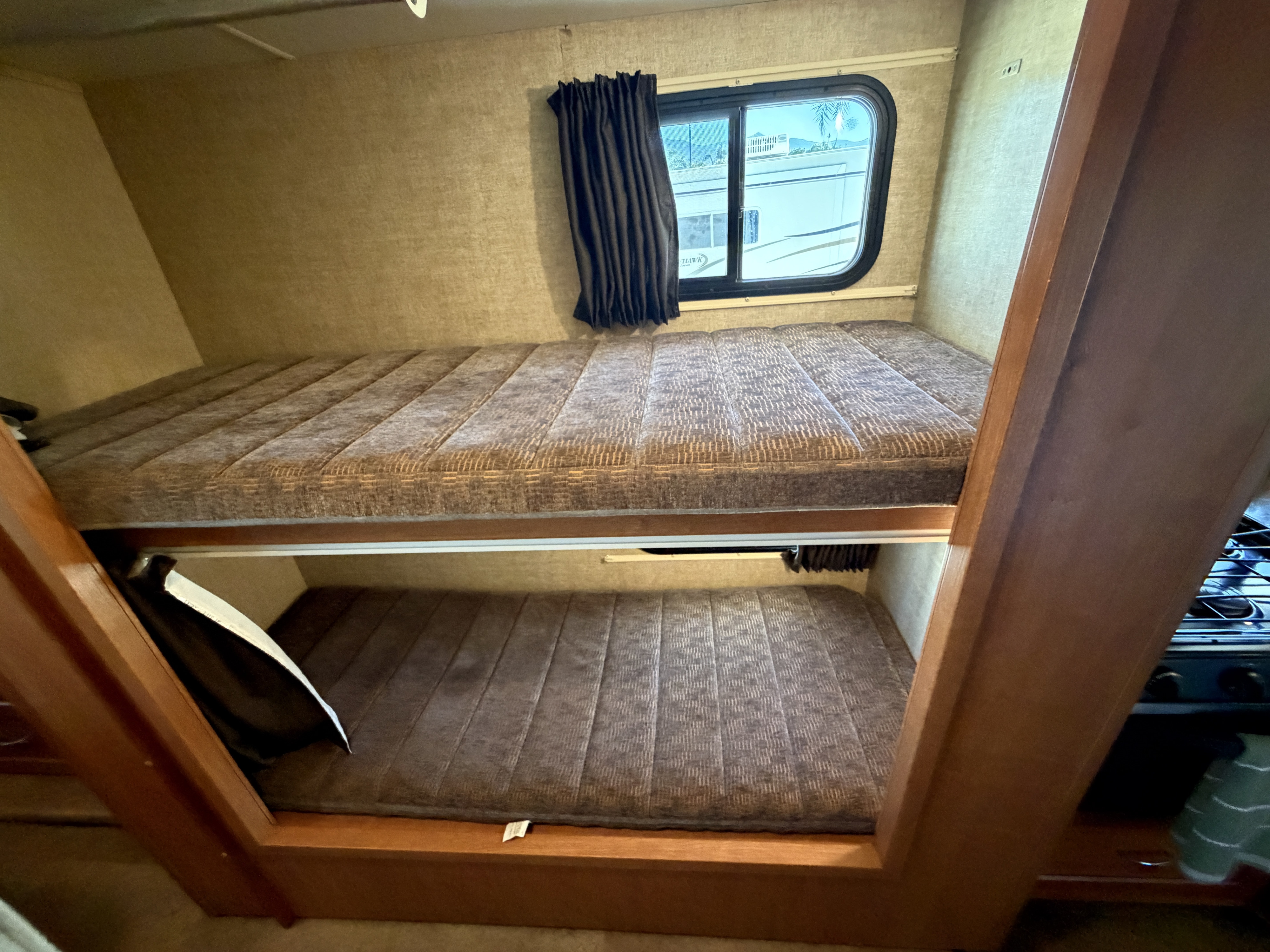 This RV rental features two cozy bunk beds with patterned mattresses, a window with curtains, and a peek of the kitchen area.. Winnebago Minnie Winnie 2017