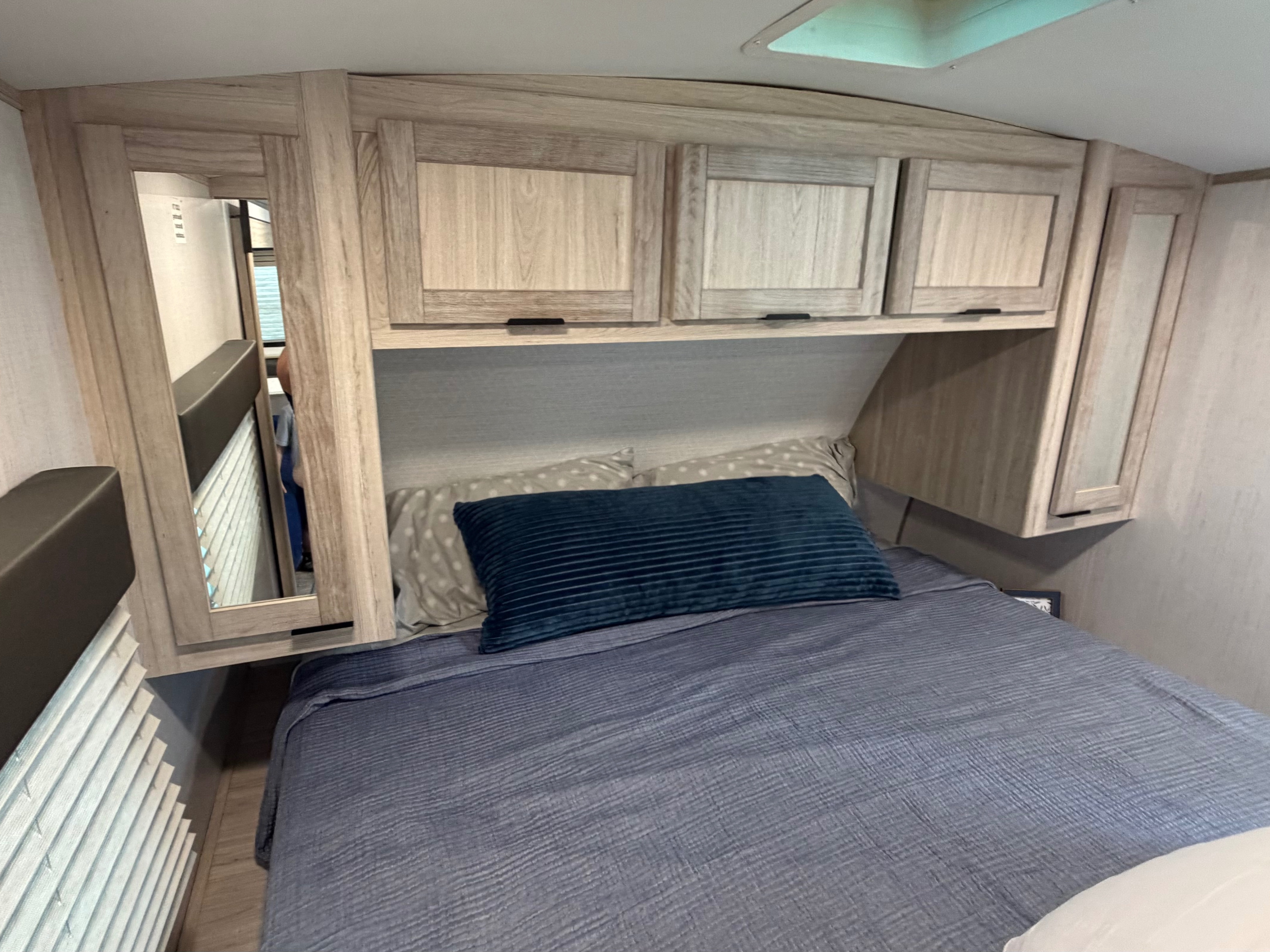 Cozy rv rental bedroom featuring a bed with blue linens, overhead wooden cabinets, and mirrored side accents.. Cruiser RV Shadow Cruiser 2022