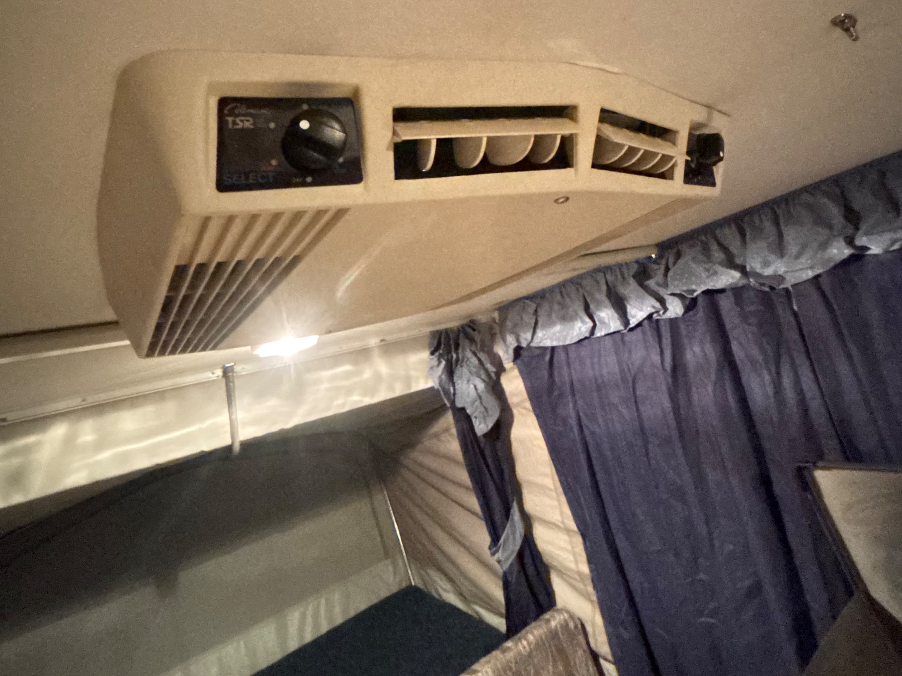 Close-up of a Coleman RV rental air conditioner unit mounted on the ceiling, showing controls and vents for cooling the camper interior.. Starcraft Travel Trailer 1994