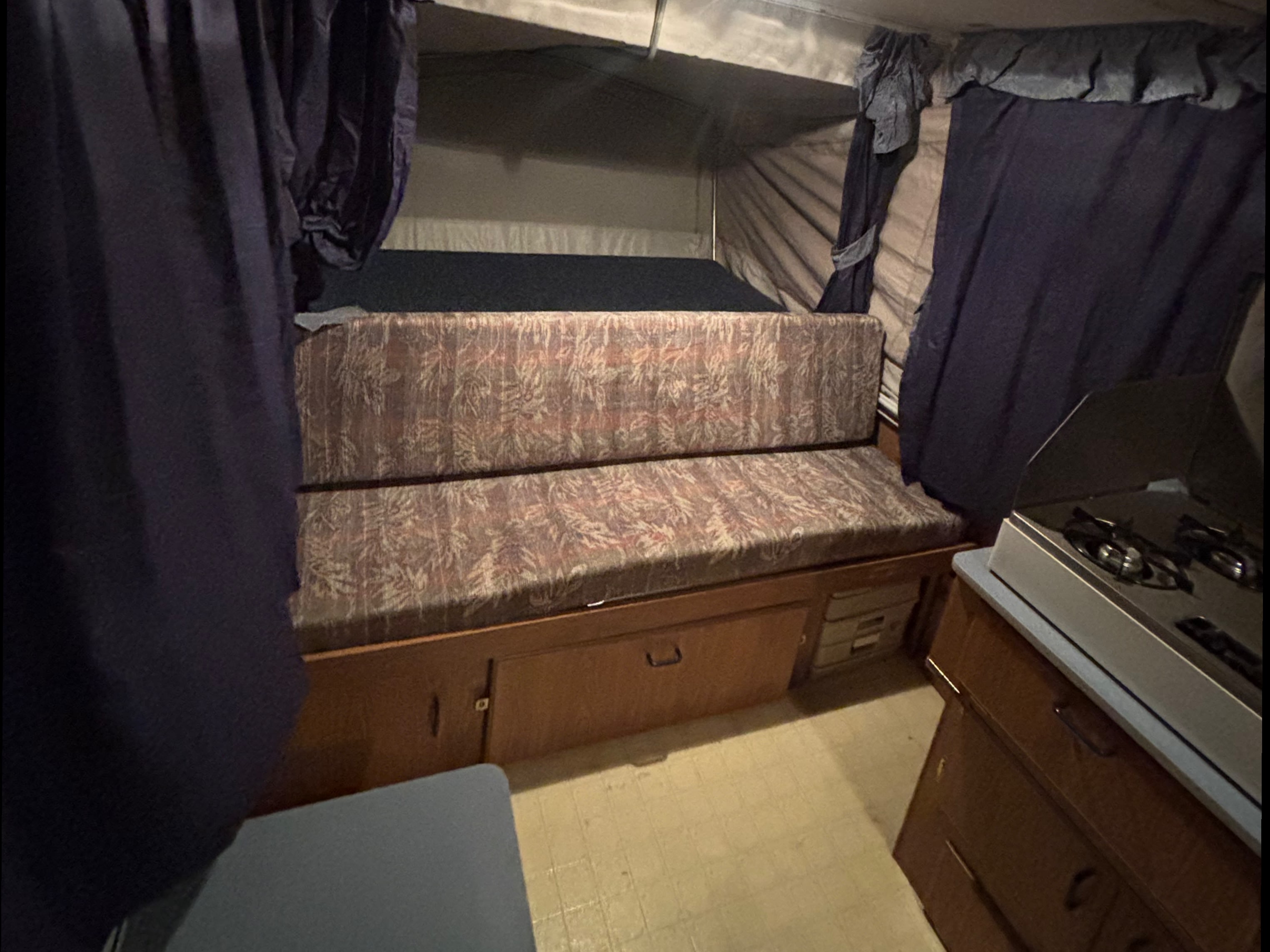 Cozy RV rental interior featuring a patterned dinette, dark privacy curtains, and a compact kitchen stovetop.. Starcraft Travel Trailer 1994