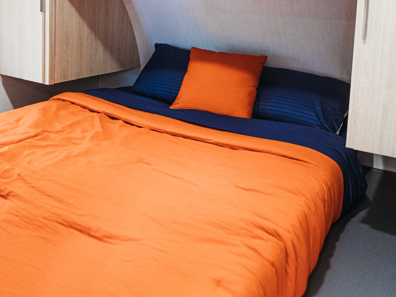 Cozy RV rental bedroom featuring vibrant orange and navy bedding, tucked into a compact space for comfortable travel.. Forest River Tracer 2024