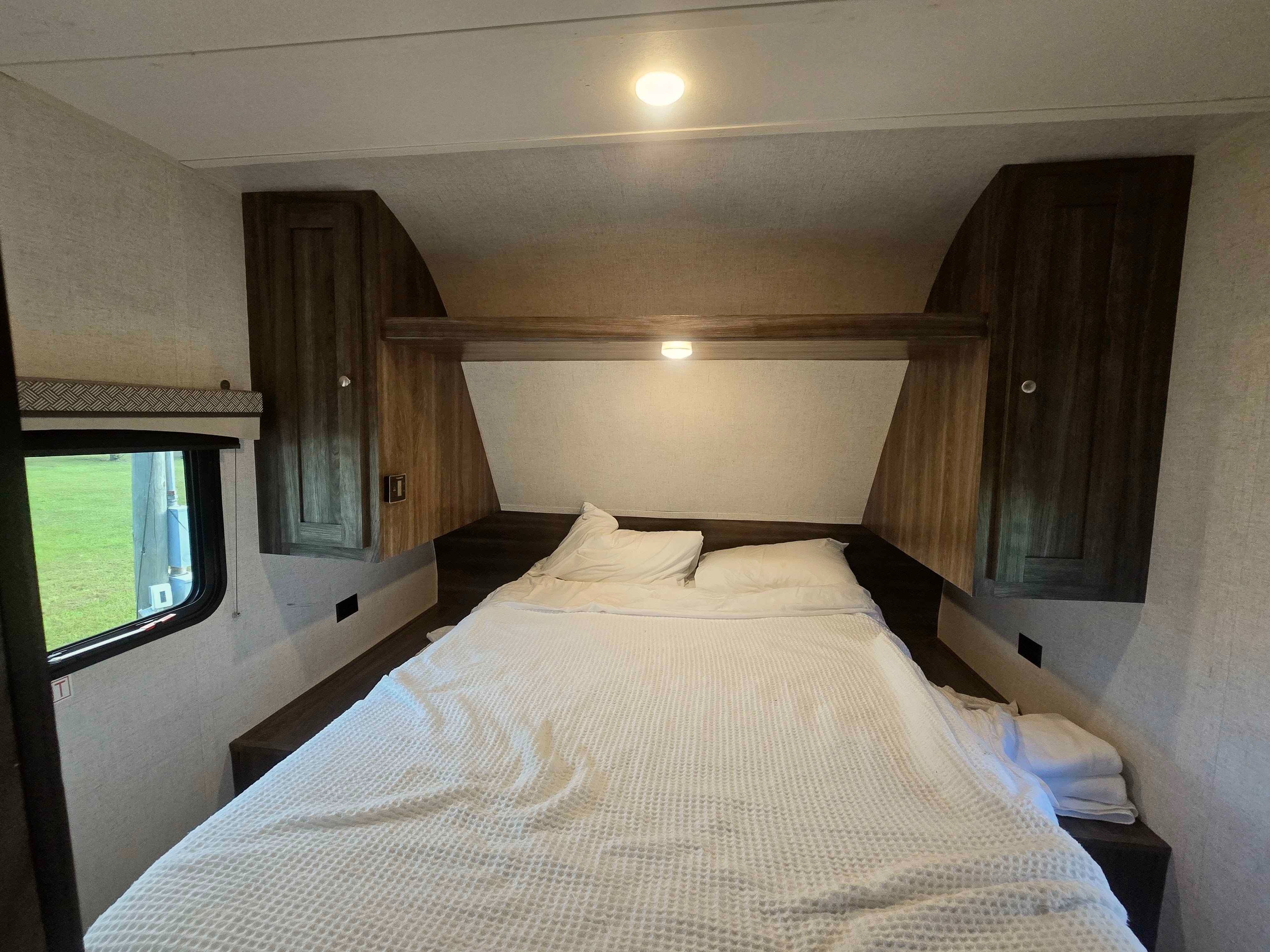 This RV rental features a cozy bedroom with white waffle-knit bedding, overhead storage, and a window on the left.. Starflyer Starcraft 2020