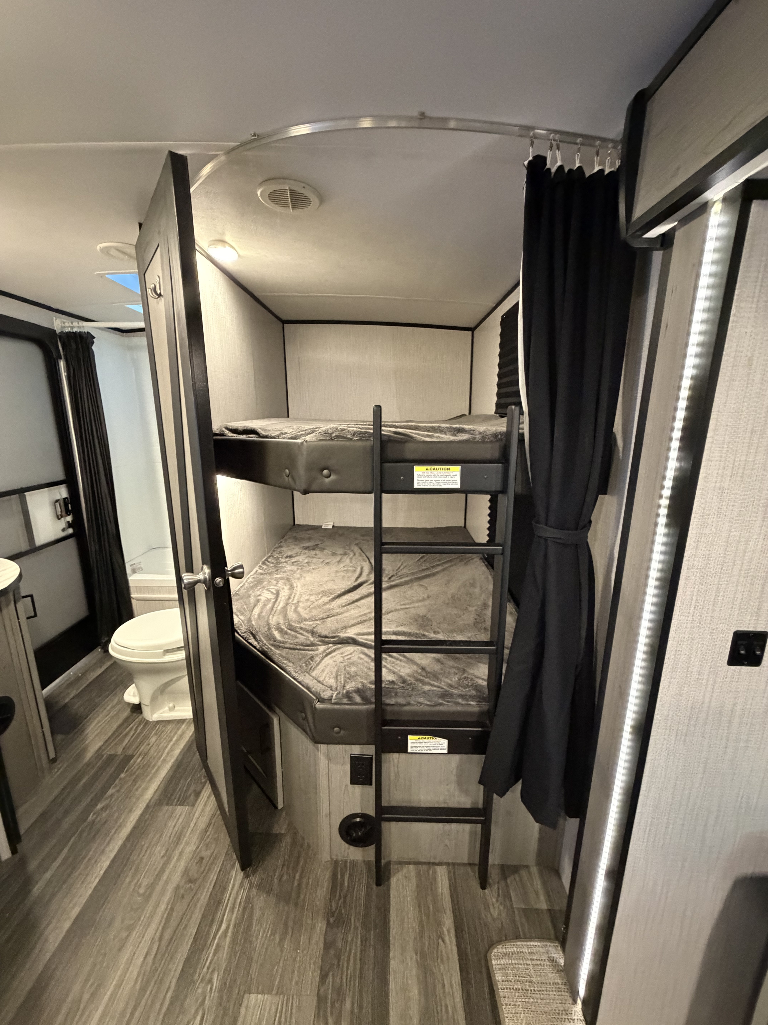 Inside an RV rental: cozy bunk beds with a ladder, and a compact bathroom featuring a toilet and shower curtain.. Heartland RVs Mallard 2021