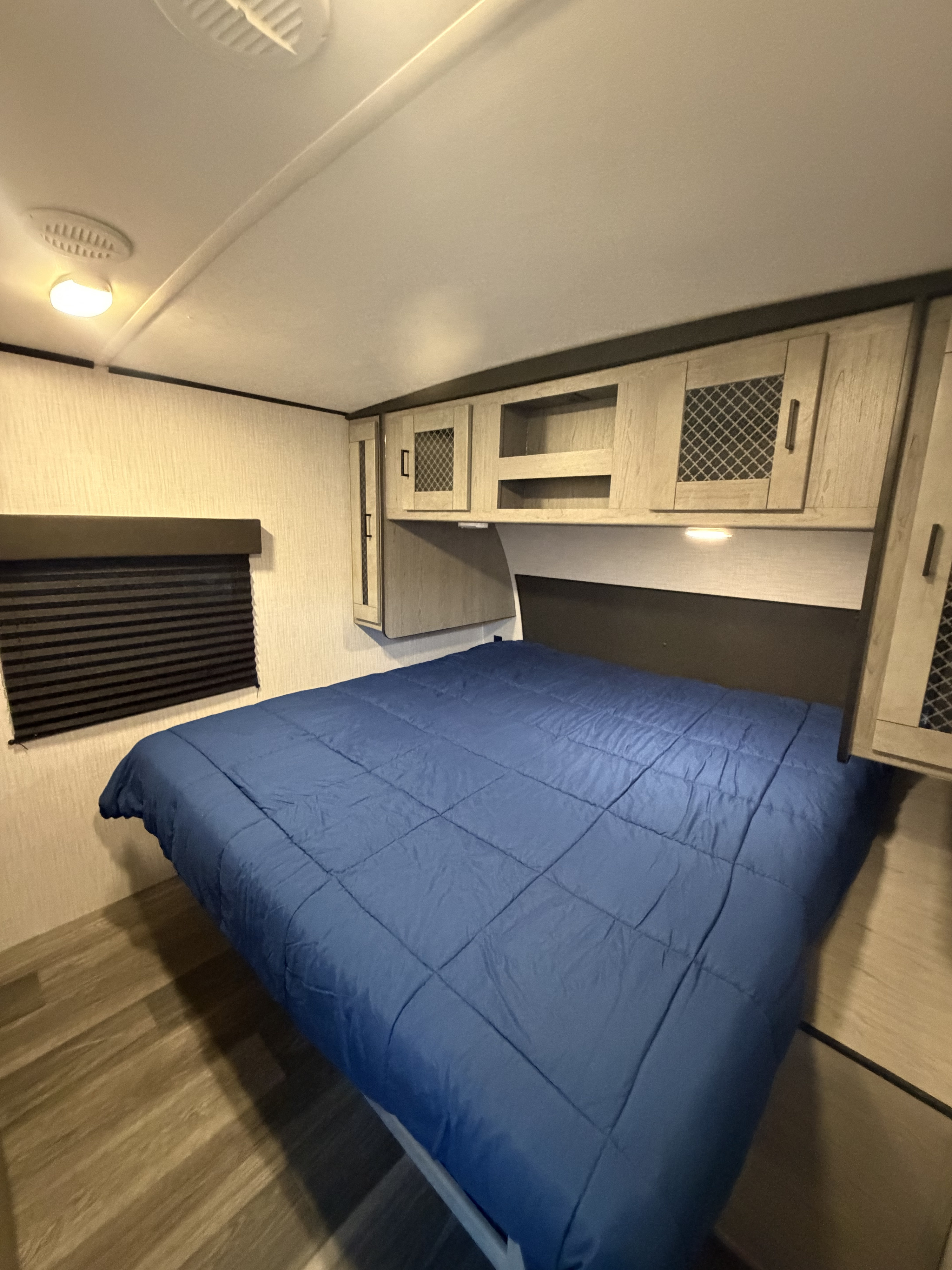 Cozy RV rental bedroom with blue comforter, overhead storage, and window blind for comfortable travel.. Heartland RVs Mallard 2021
