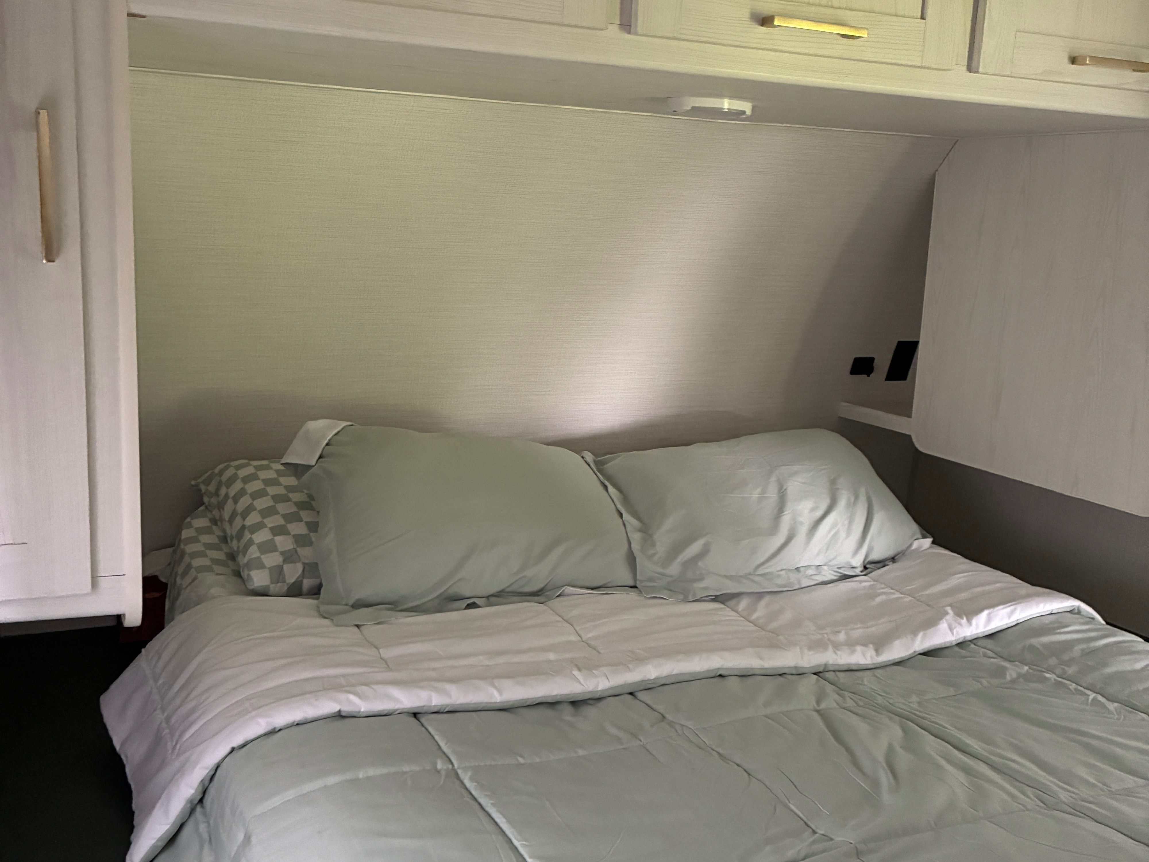 Cozy RV rental bedroom featuring a comfortable bed with light green bedding, overhead storage, and an integrated light fixture.. Heartland RVs Eddie Bauer 2024