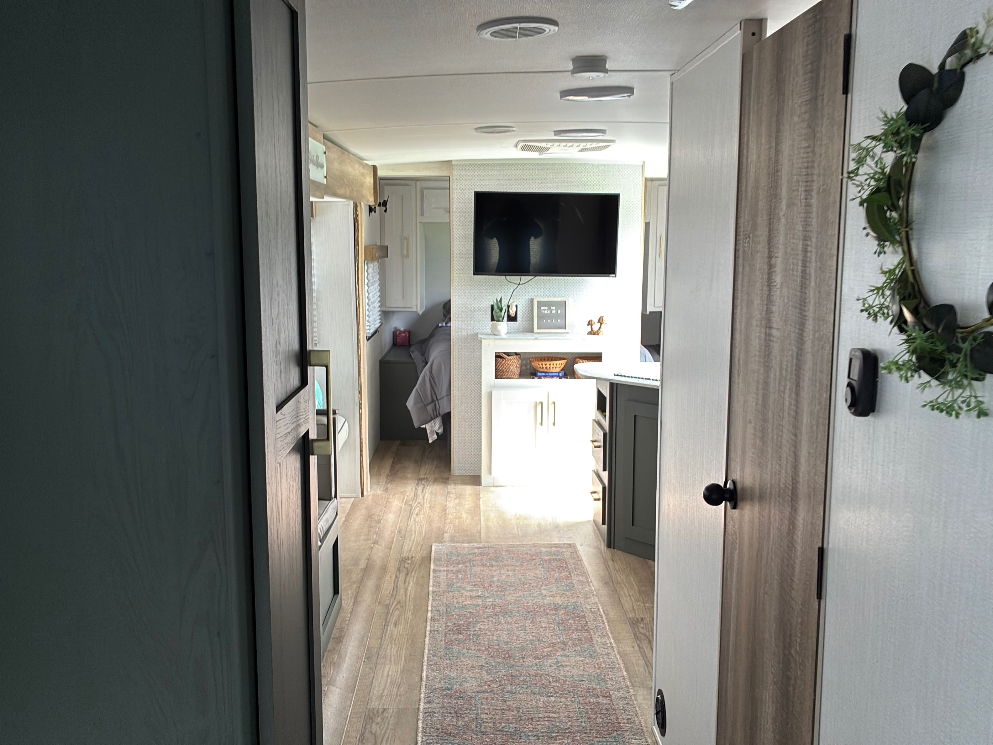 Inside a modern RV rental: a hallway view showing the living space, bedroom, and contemporary decor with a TV and rug.. Heartland RVs Eddie Bauer 2024