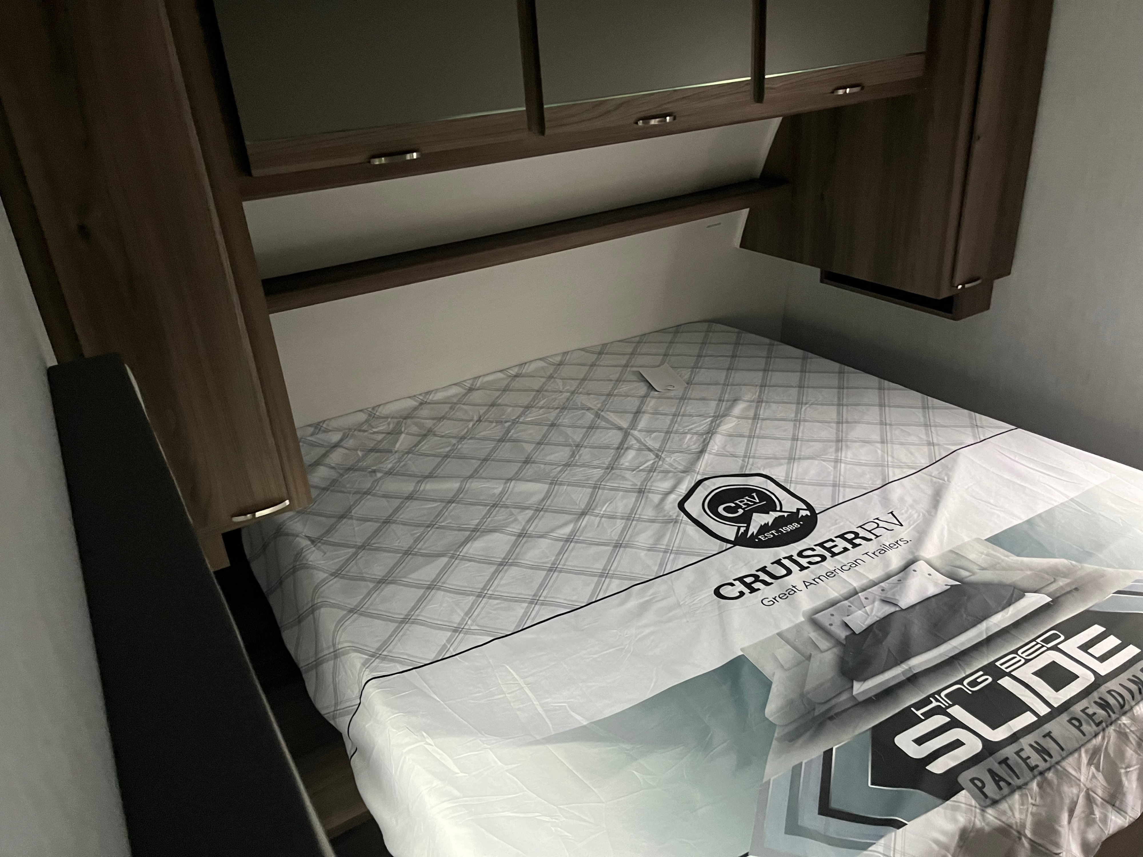 This RV rental bedroom features a King Bed Slide mattress by Cruiser RV, surrounded by wooden cabinets and shelving.. Cruiser RV Radiance 2023