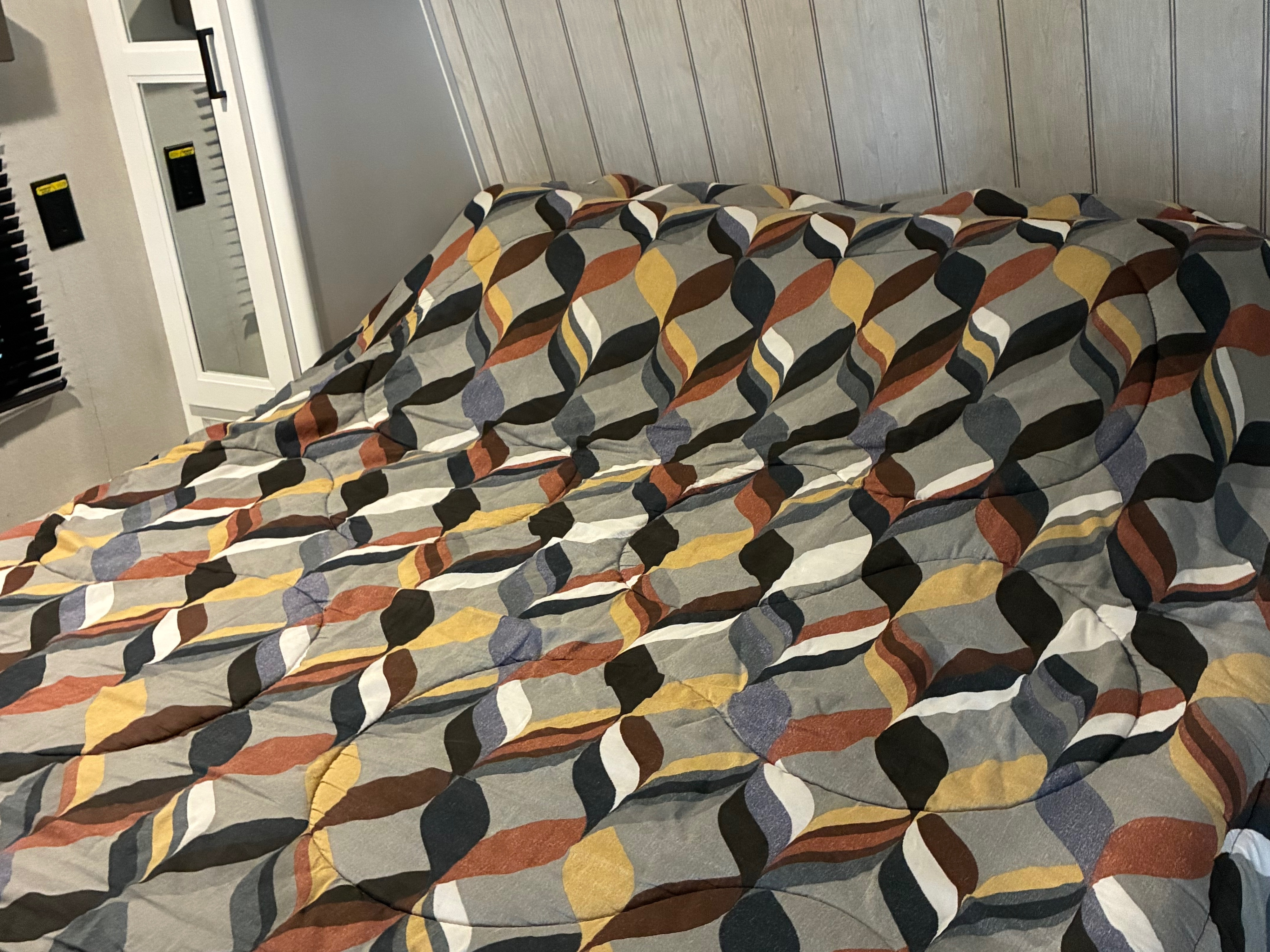 RV rental cozy bedroom with a striking abstract patterned comforter in grey, yellow, brown, and blue tones.. Keystone RV Hideout 2022