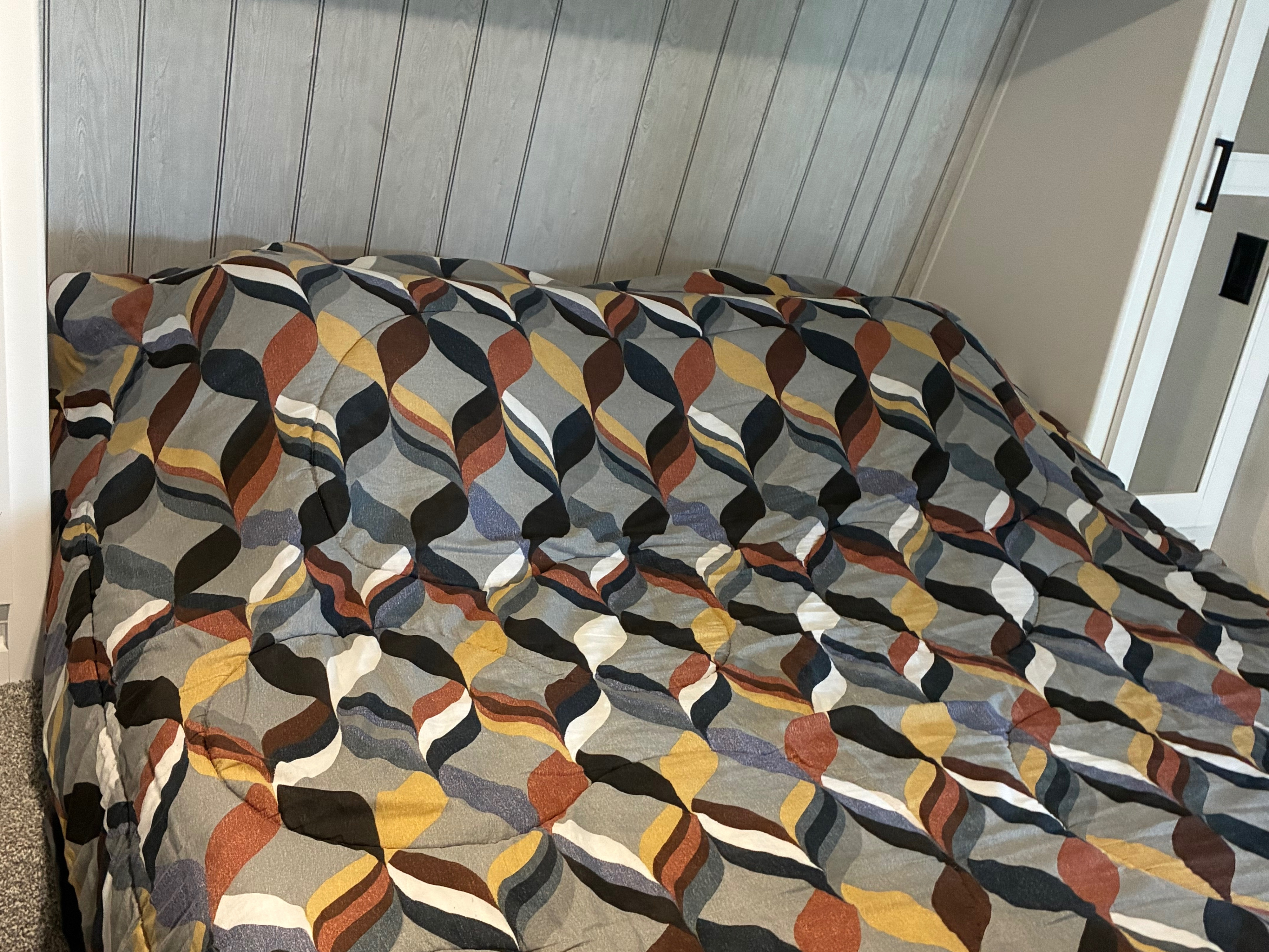 Cozy RV rental bed featuring a colorful, patterned comforter and light wood-paneled wall, perfect for a comfortable stay.. Keystone RV Hideout 2022