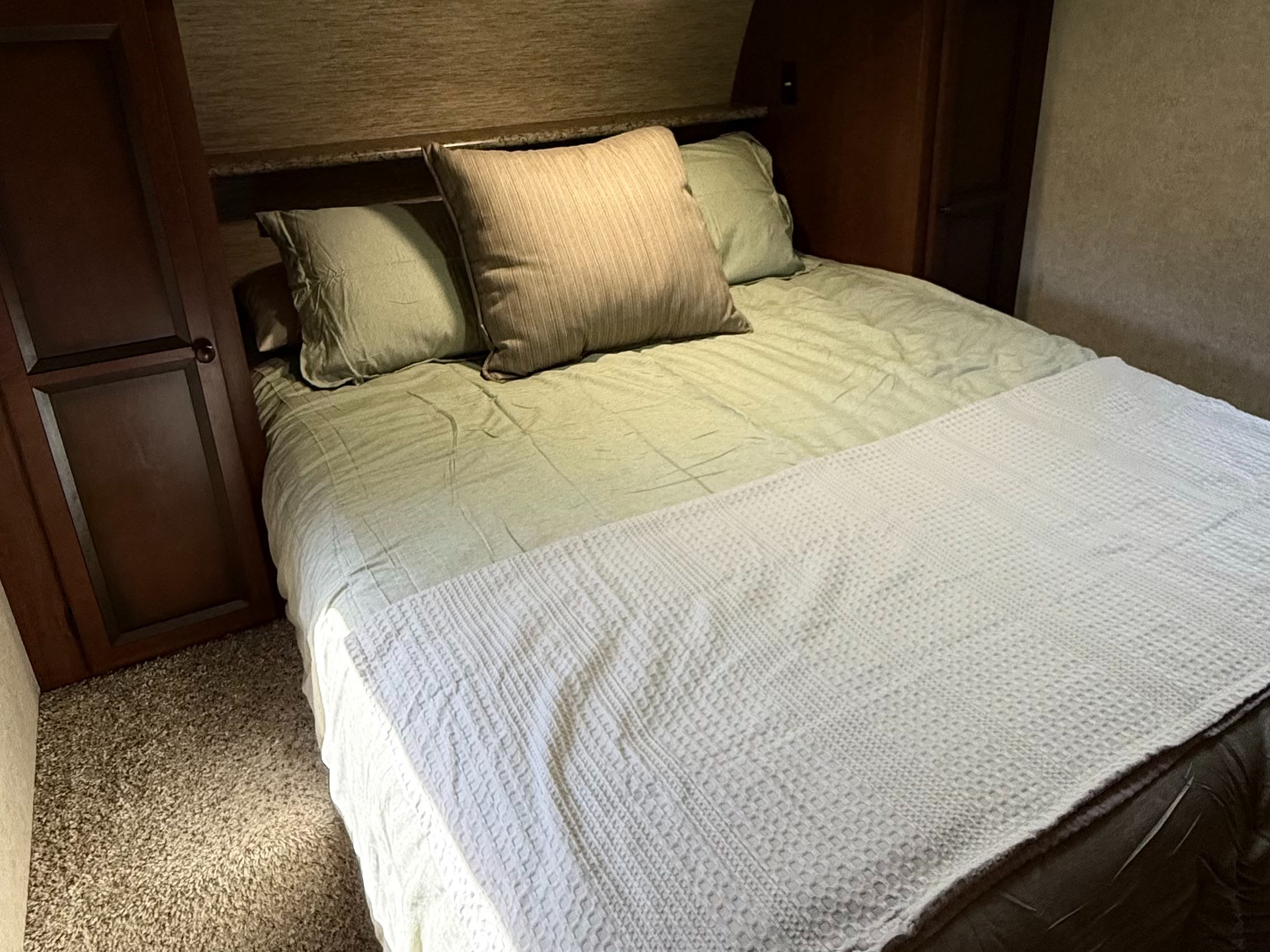 Inviting RV rental bedroom features a neatly made bed with green linens, pillows, and wooden storage on the left.. Palomino Solaire 2013
