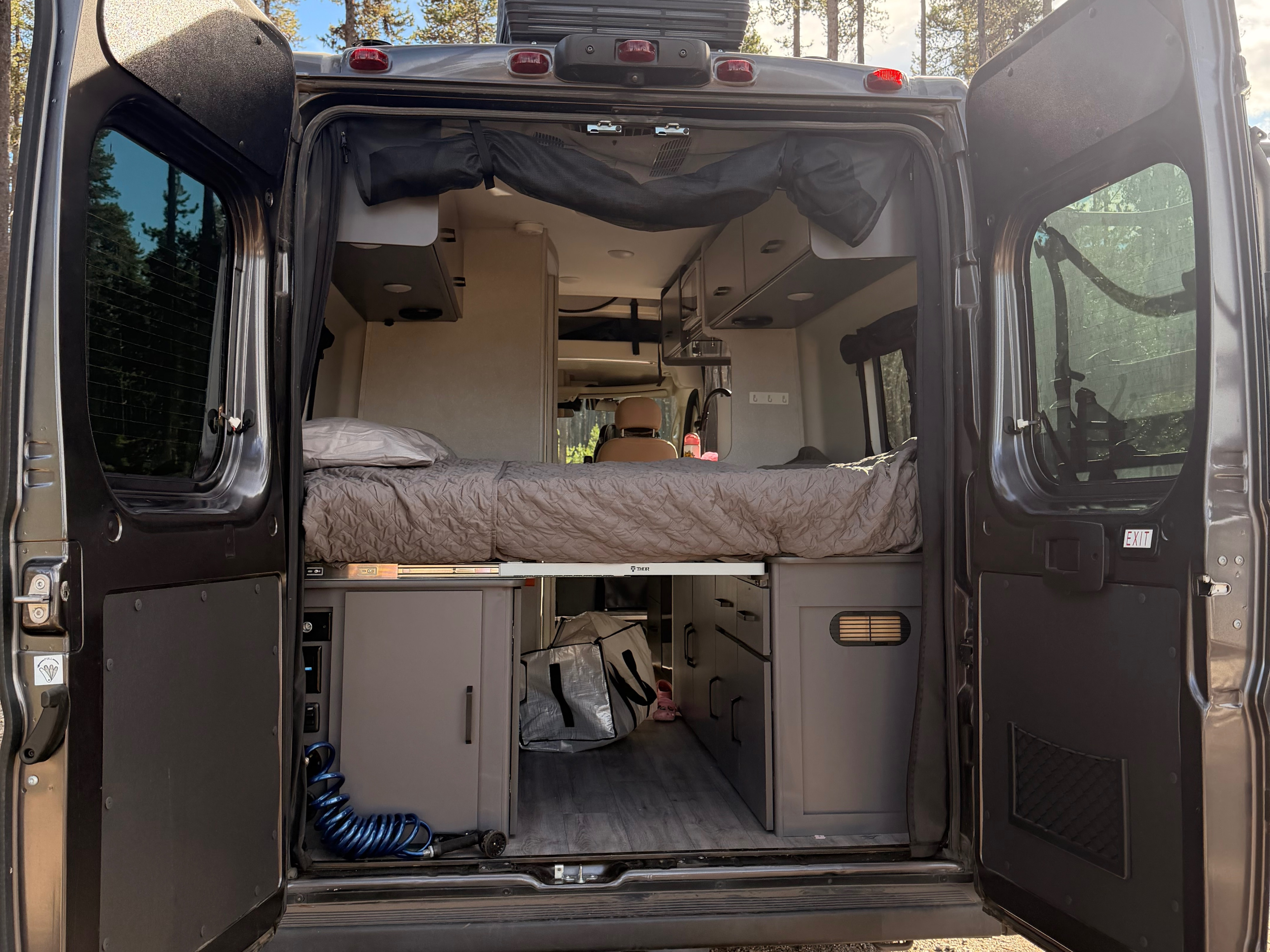 Rear view of an RV rental's cozy campervan interior, featuring a bed, storage cabinets, and a hose, set for outdoor adventures.. Thor Motor Coach Dazzle 2AB 2023