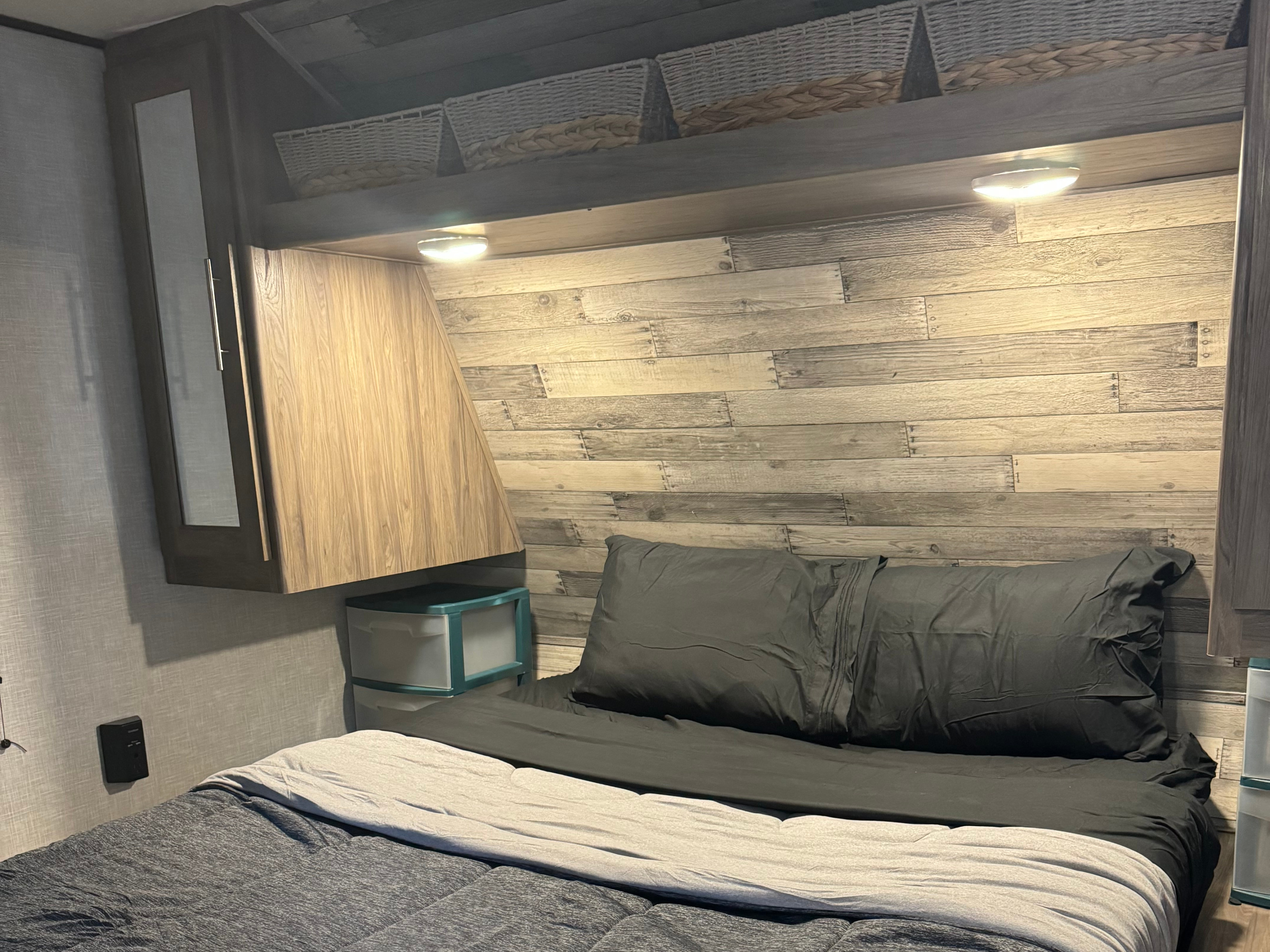 Cozy RV rental bedroom with a wood-accent wall, dark bedding, overhead storage, and under-cabinet lighting.. Crossroads RV Zinger 2022