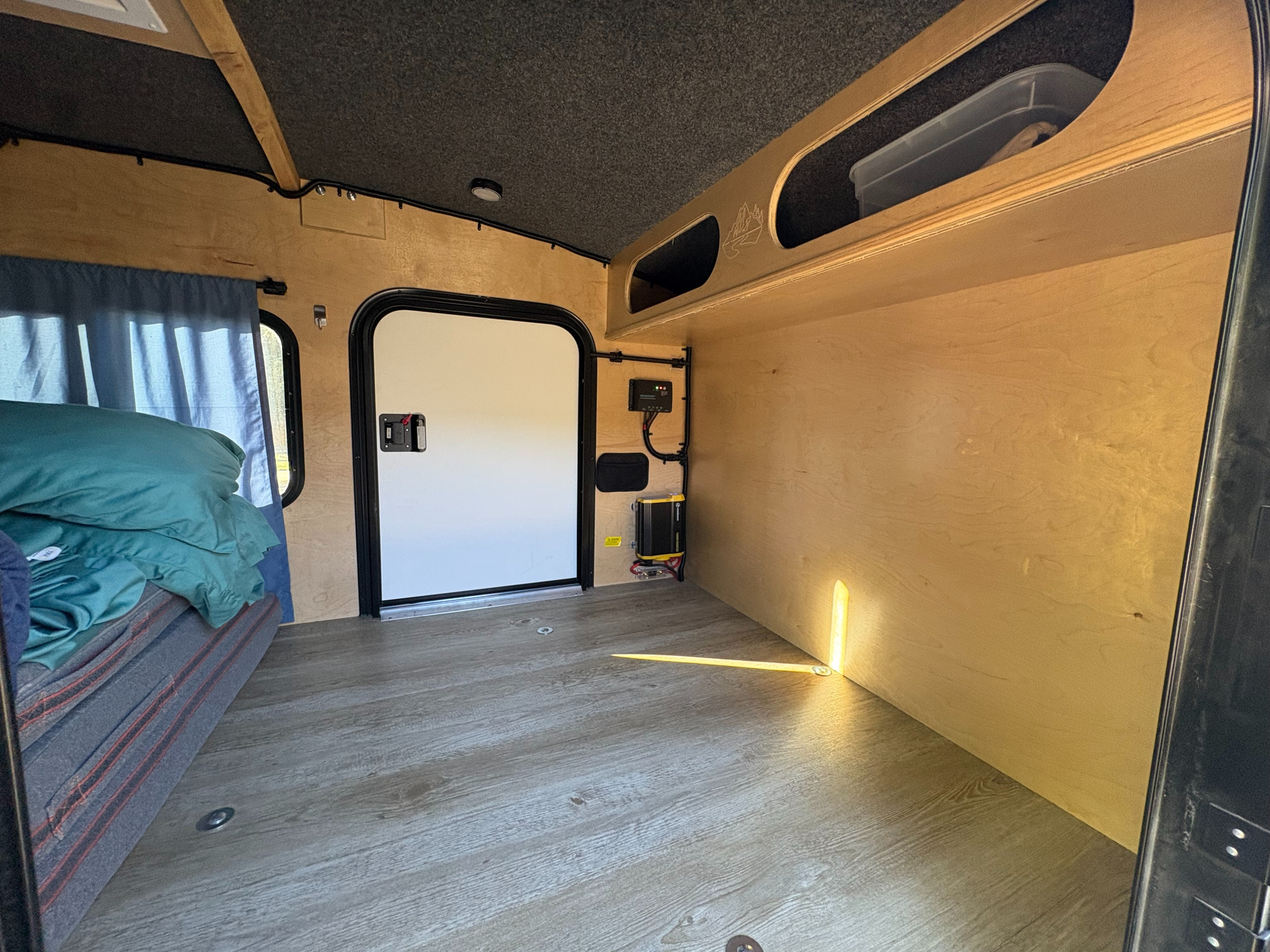 This RV rental interior features a cozy bed, wooden walls, storage shelves, and visible electrical components, perfect for a camper adventure.. Outbound Trailers Outbound Extreme 2023
