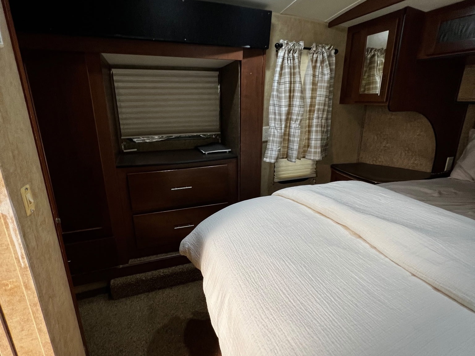 Cozy RV rental bedroom with white bedding, wood cabinetry, and plaid curtains, offering a comfortable stay.. Dutchmen Komfort 3130 FRL 2011