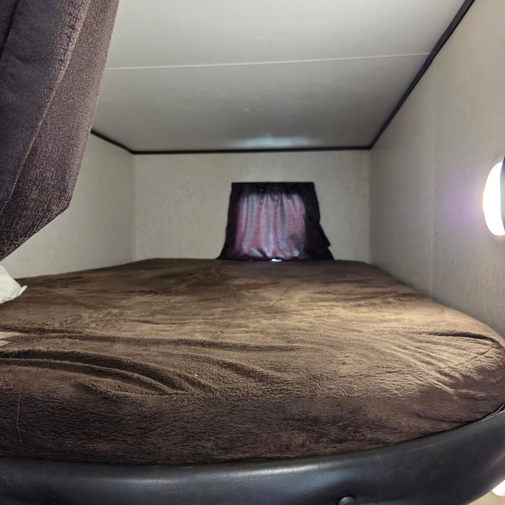 Experience comfort in this RV rental's cozy bunk, complete with a soft brown blanket, window, and wall light.. Jayco Jay Flight SLX Rocky Mtn Edition 2019