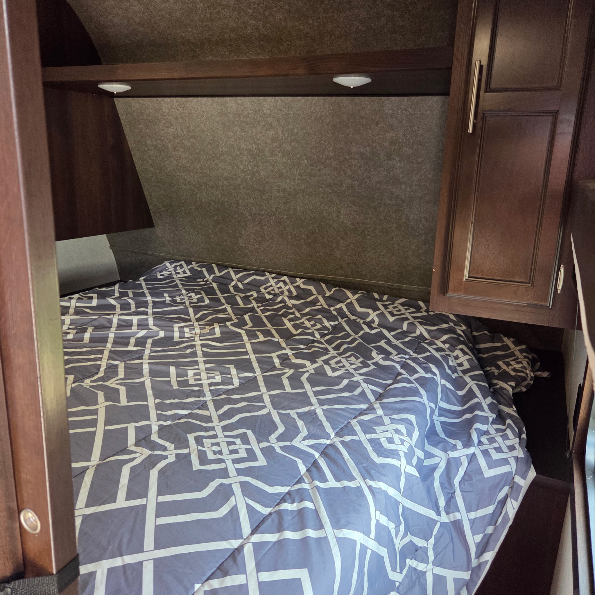 Cozy RV rental bedroom featuring a bed with a blue and white geometric patterned comforter, wooden storage, and reading lights.. Jayco Jay Flight SLX Rocky Mtn Edition 2019