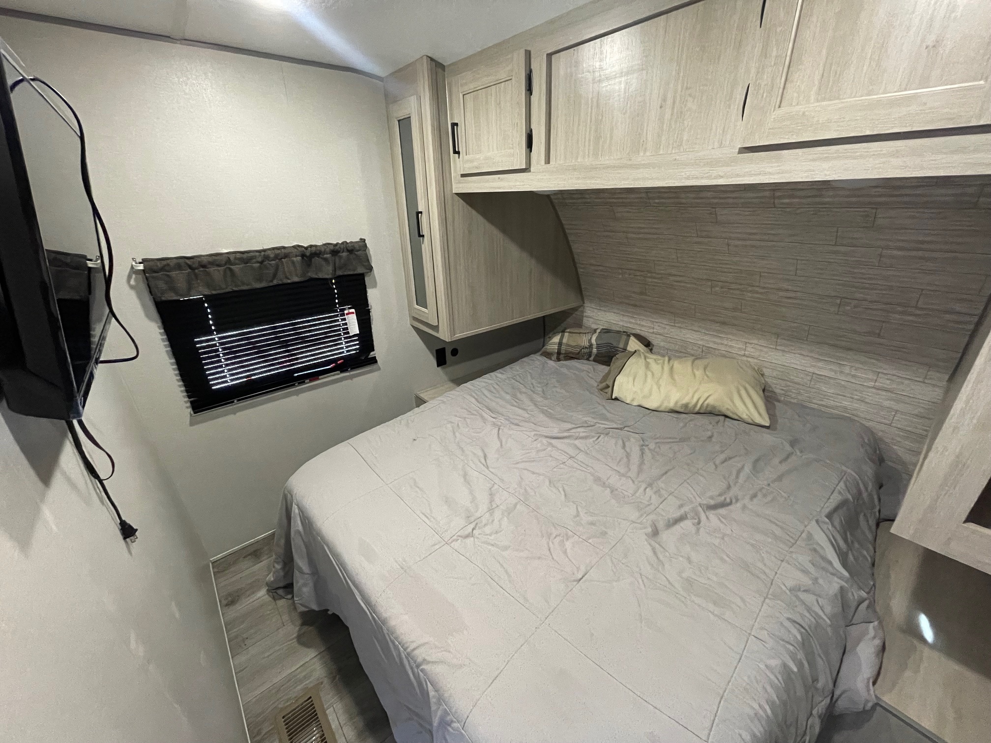Cozy RV rental bedroom featuring a comfy bed, overhead cabinets, window with blinds, and TV, perfect for travel comfort.. Coachmen Catalina Legacy Edition 2024