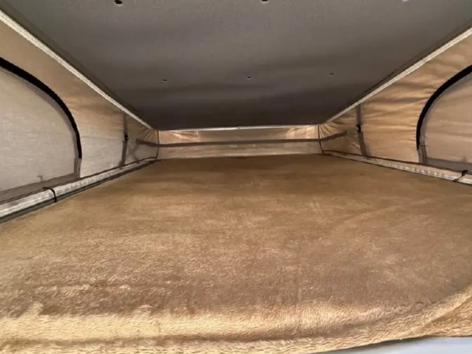 Inside a pop-top RV rental: a plush, tan sleeping platform under a dark gray ceiling, surrounded by light fabric walls, ideal for camping.. Thor Dazzle 2024