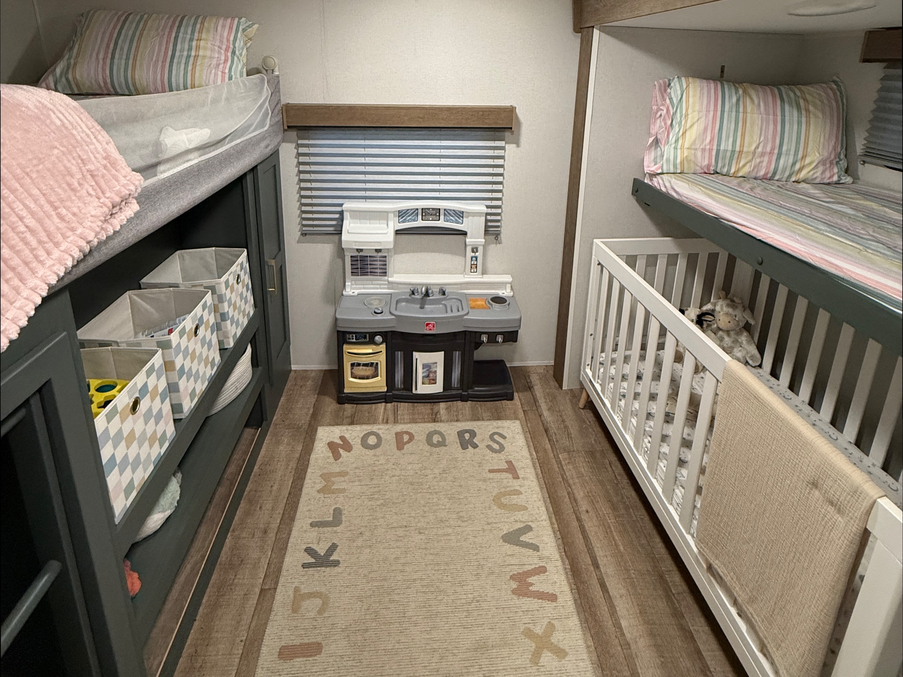 Cozy RV rental interior with bunk beds, a crib, toy kitchen, and an alphabet rug, perfect for family adventures.. Heartland RVs Eddie Bauer 2026