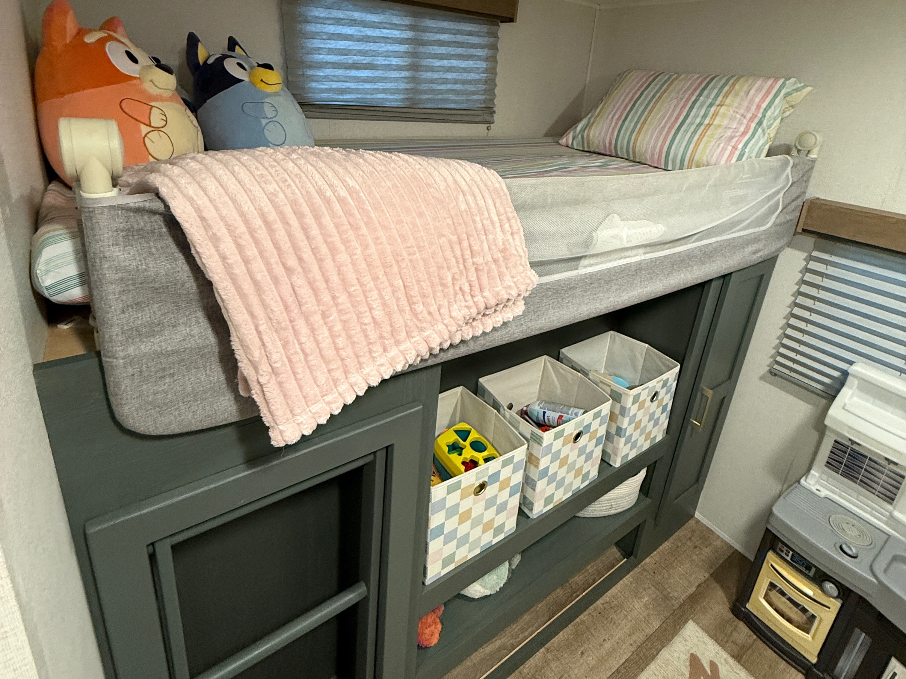 A cozy bunk bed in an RV rental, featuring stuffed animals, a pink blanket, and organized toy storage beneath for kids.. Heartland RVs Eddie Bauer 2026
