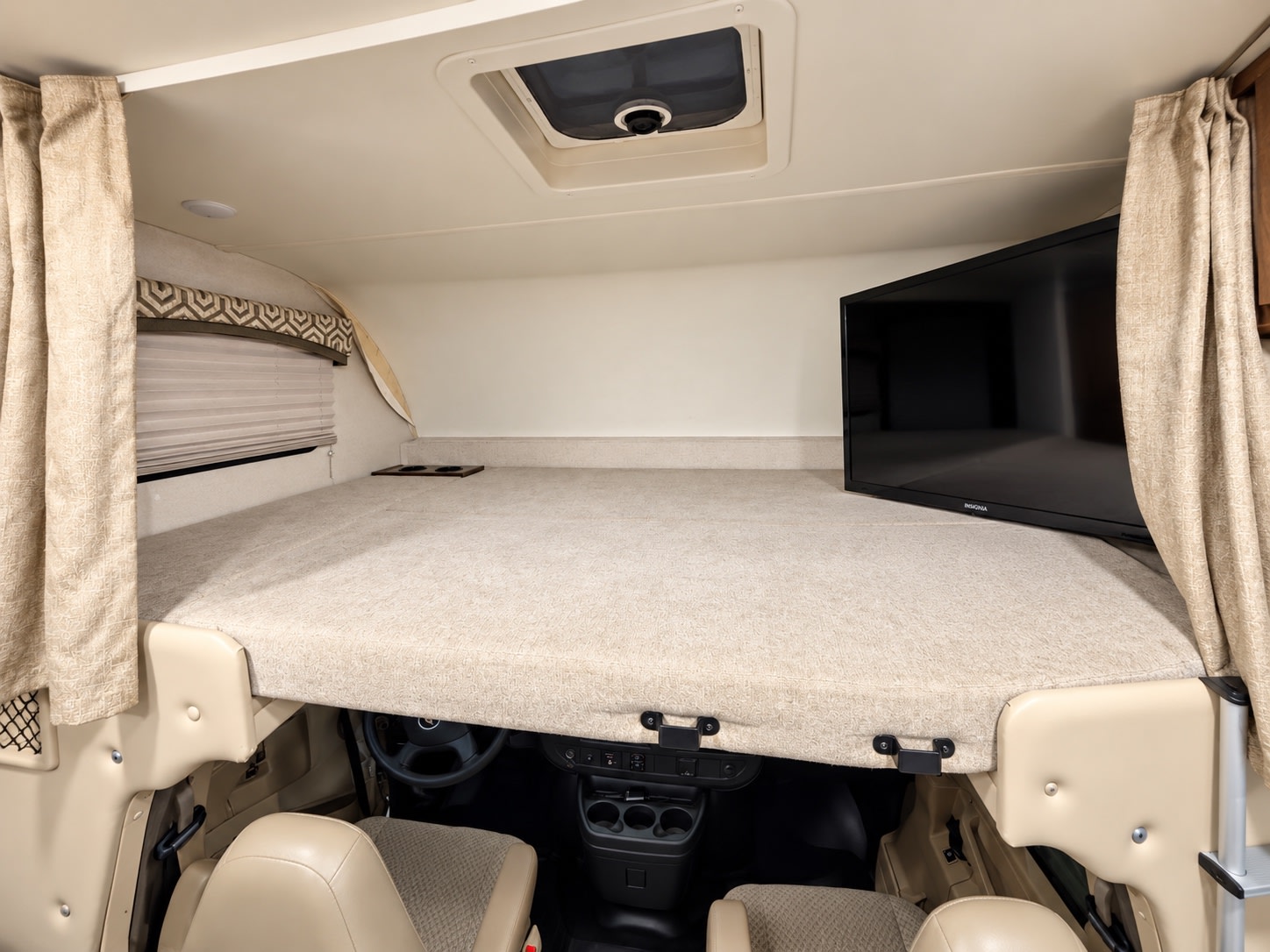 RV rental cab-over bunk sleeping area with TV, above the driver's cockpit. Features light-toned interior and blinds for privacy.. Thor Chateau 2020