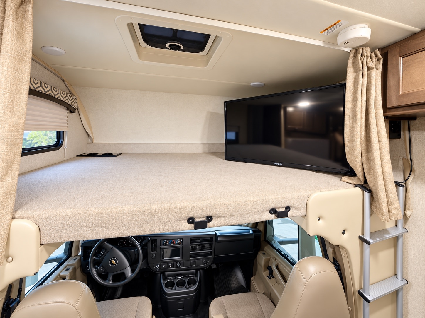 Overhead bunk bed with TV in an rv rental. View shows the driver's cab below, a side window, and an access ladder.. Thor Chateau 2020