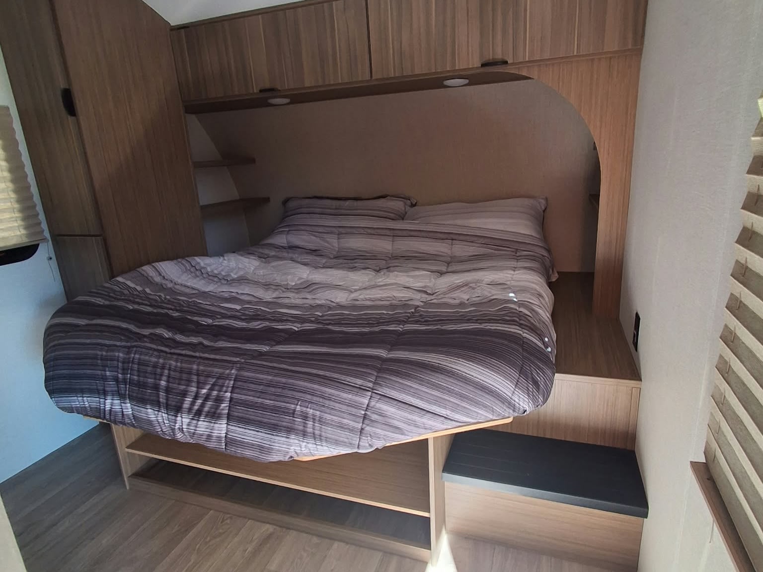 Cozy RV rental bedroom interior featuring a comfy bed with striped bedding, overhead storage, and built-in shelving.. Forest River Salem FSX 2026