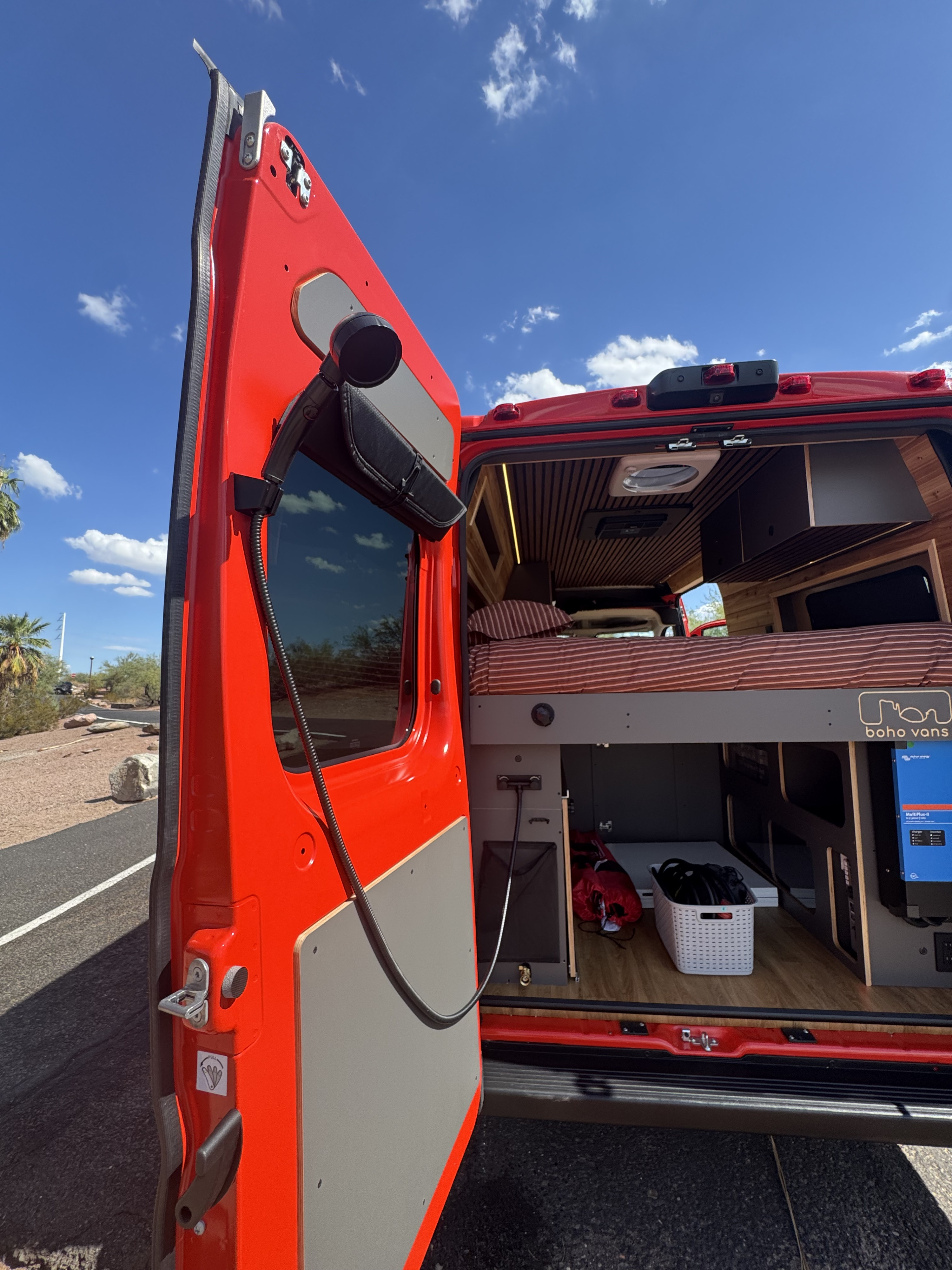 Explore this open red Boho Vans RV rental, showcasing a comfortable interior with a bed, storage, and electrical system for road trips.. Ram Promaster 2023