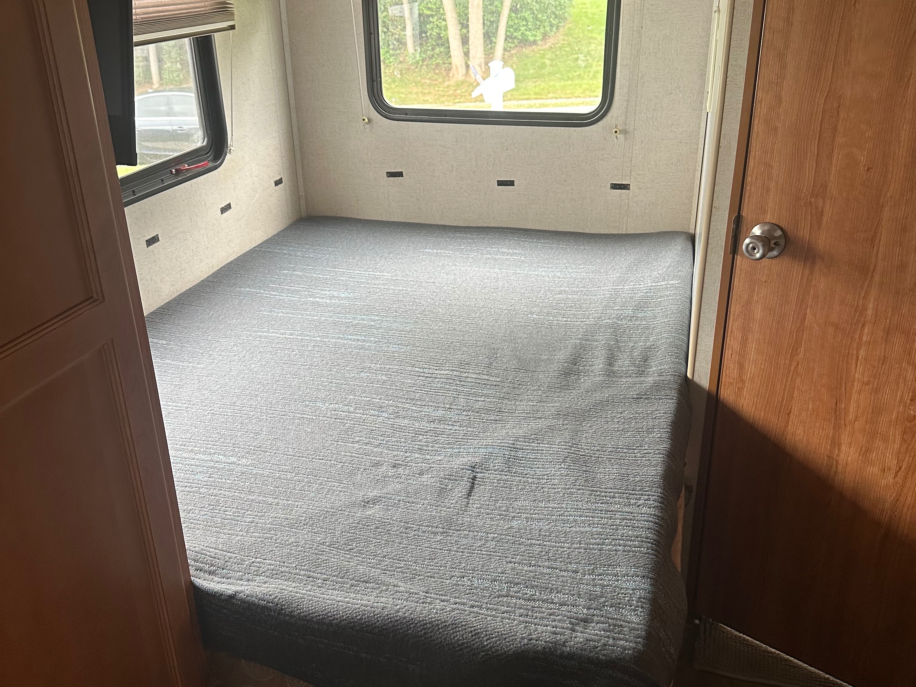 Inside this RV rental bedroom: a neatly made gray bed, a window with an outdoor view, and a wooden door.. Fleetwood Other 2010