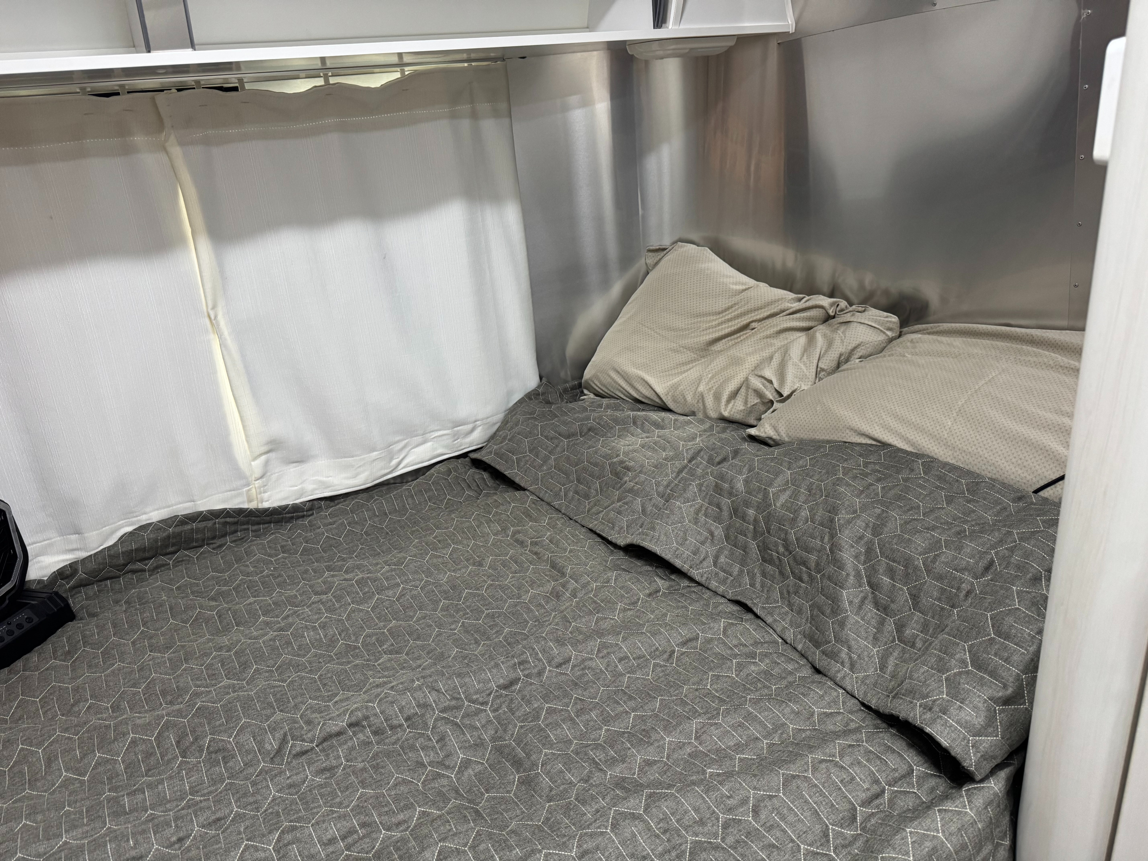Cozy RV rental bedroom with a neatly made bed featuring a grey hexagonal patterned duvet, light pillows, and privacy curtains.. Airstream Sport 2019