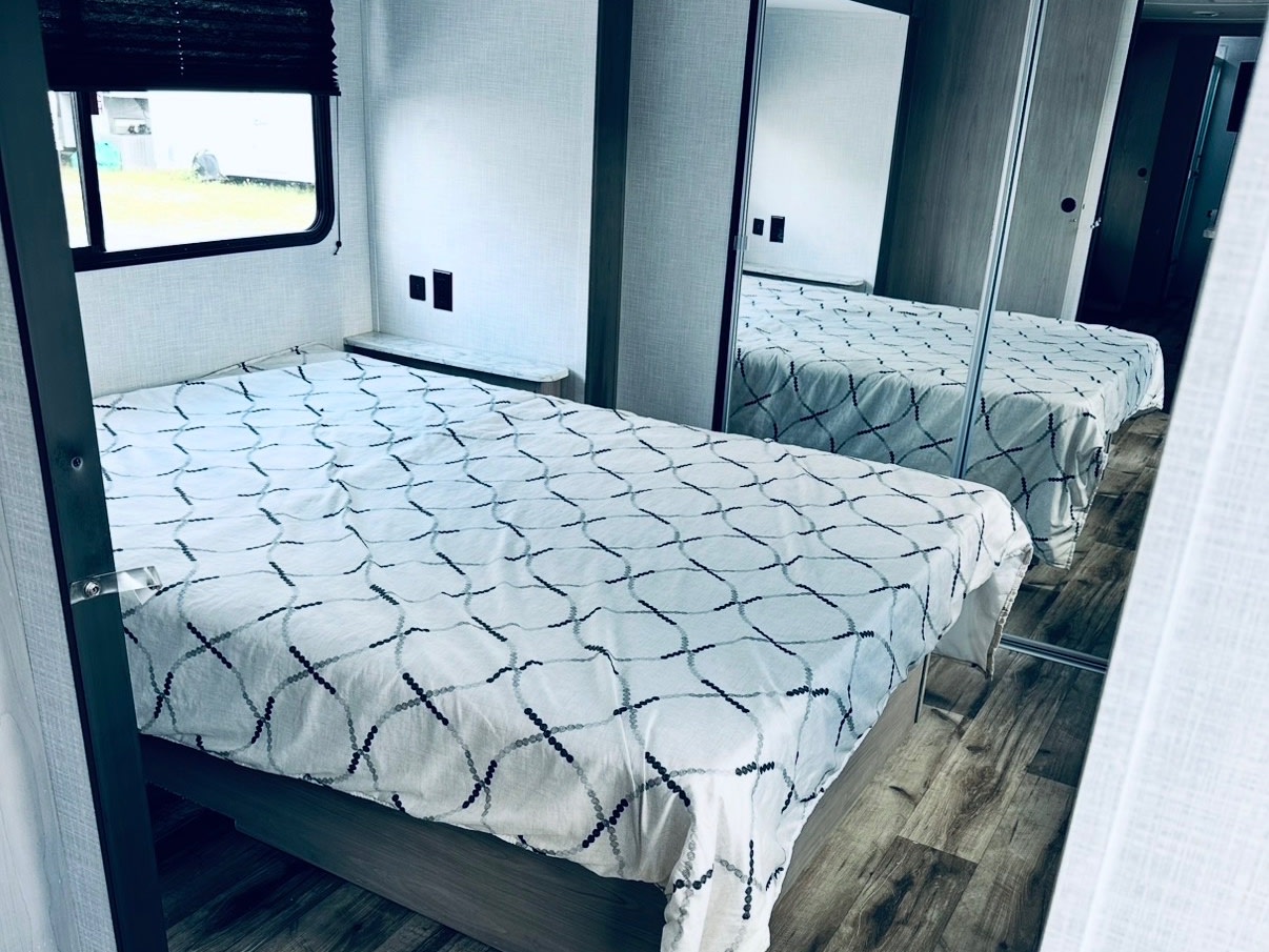 Modern rv rental bedroom with a neatly made bed, window, and mirrored closet, reflecting the clean interior space.. Coleman Light 2022