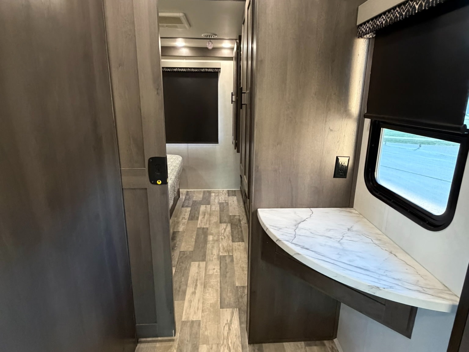 Modern rv rental interior: hallway leading to a bed, with wood paneling, a marble counter, and a window on the right.. FR3 FR3 Motorhome 2022