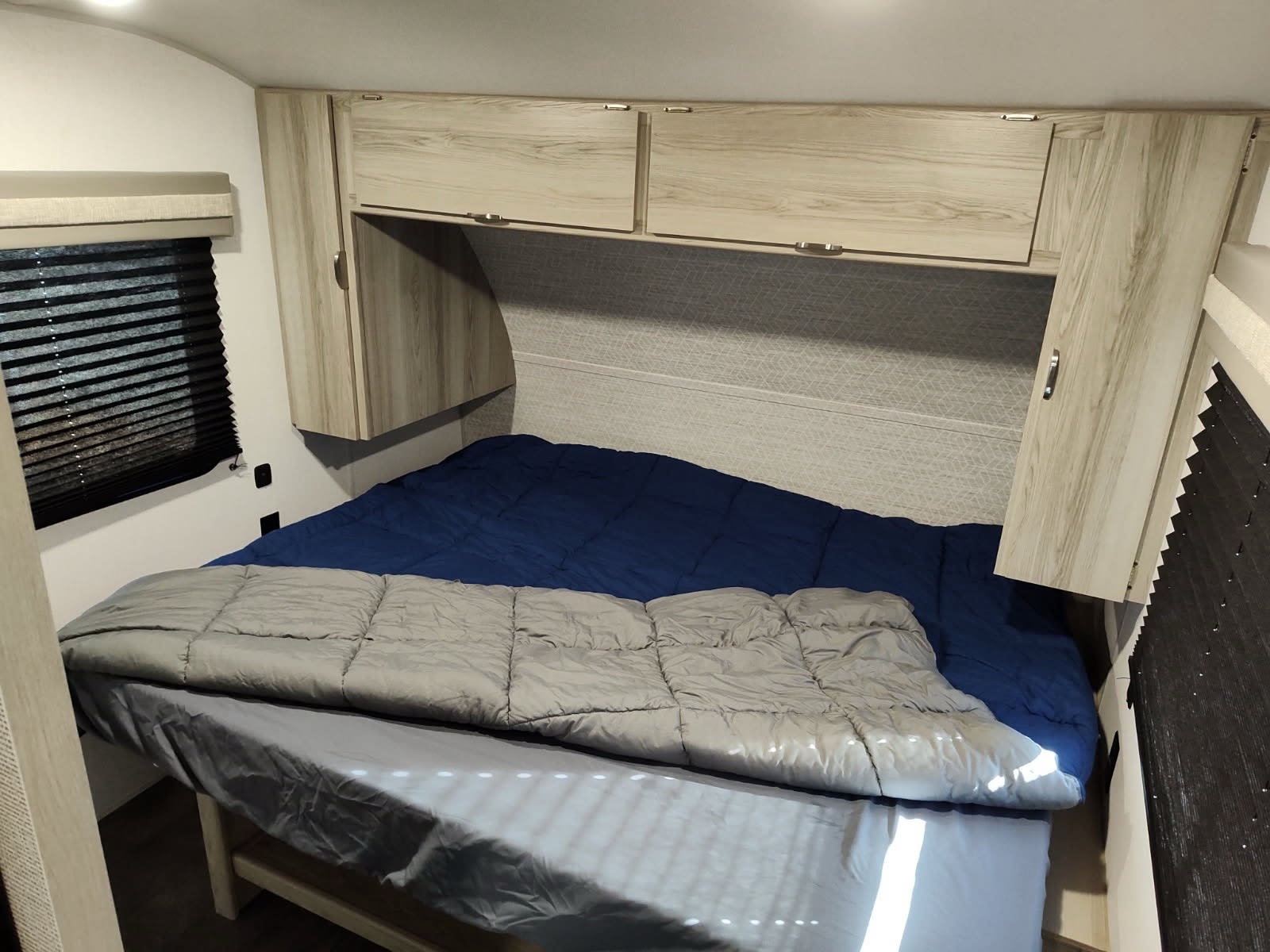 Compact RV rental bedroom featuring a comfortable bed, overhead storage, and a window with blinds.. Forest River Wildwood FSX 2024