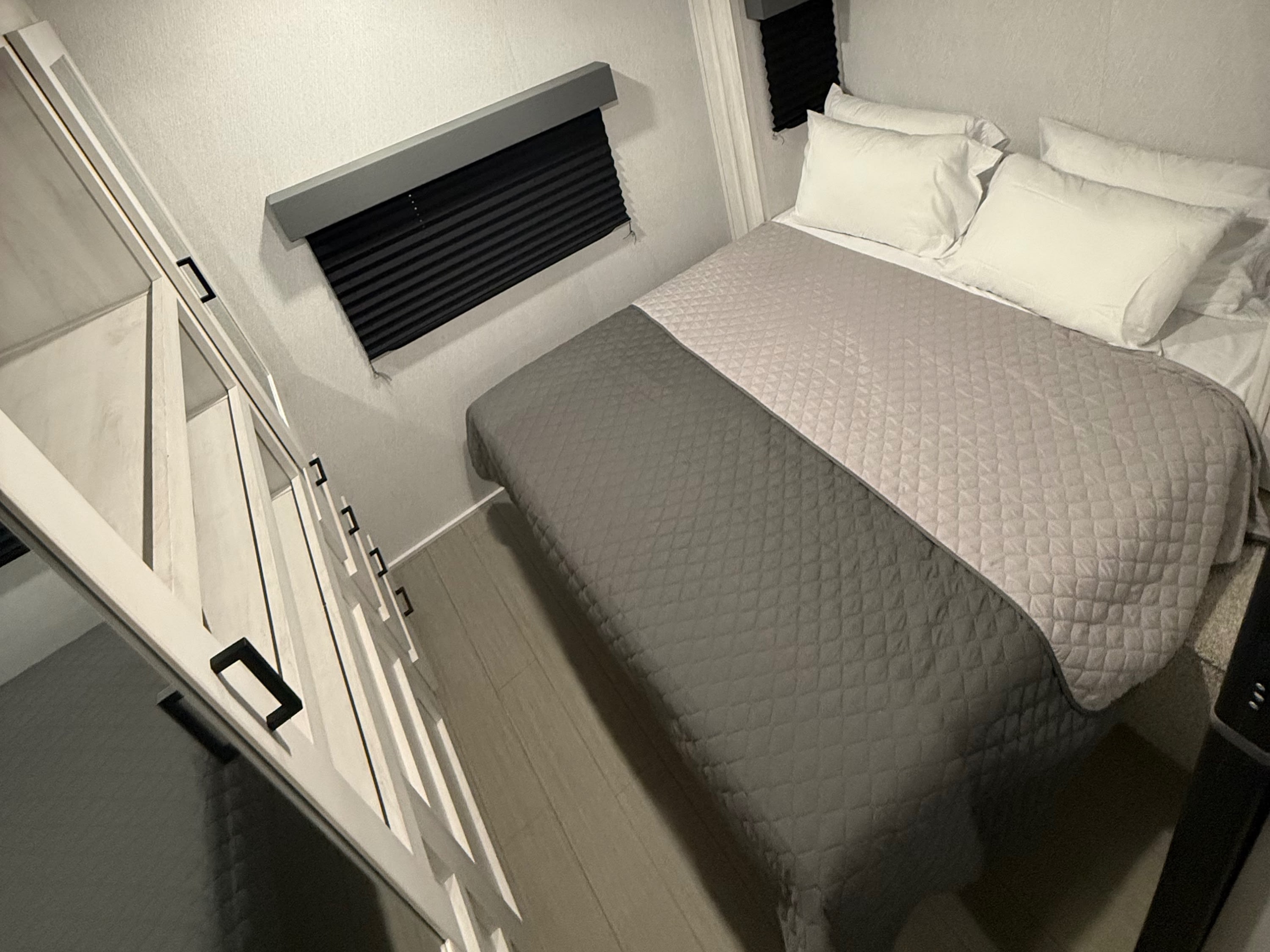 Modern RV rental bedroom: comfy bed, overhead storage, window blinds, and stairs. Your cozy retreat on wheels awaits!. East to West Entrada 2025