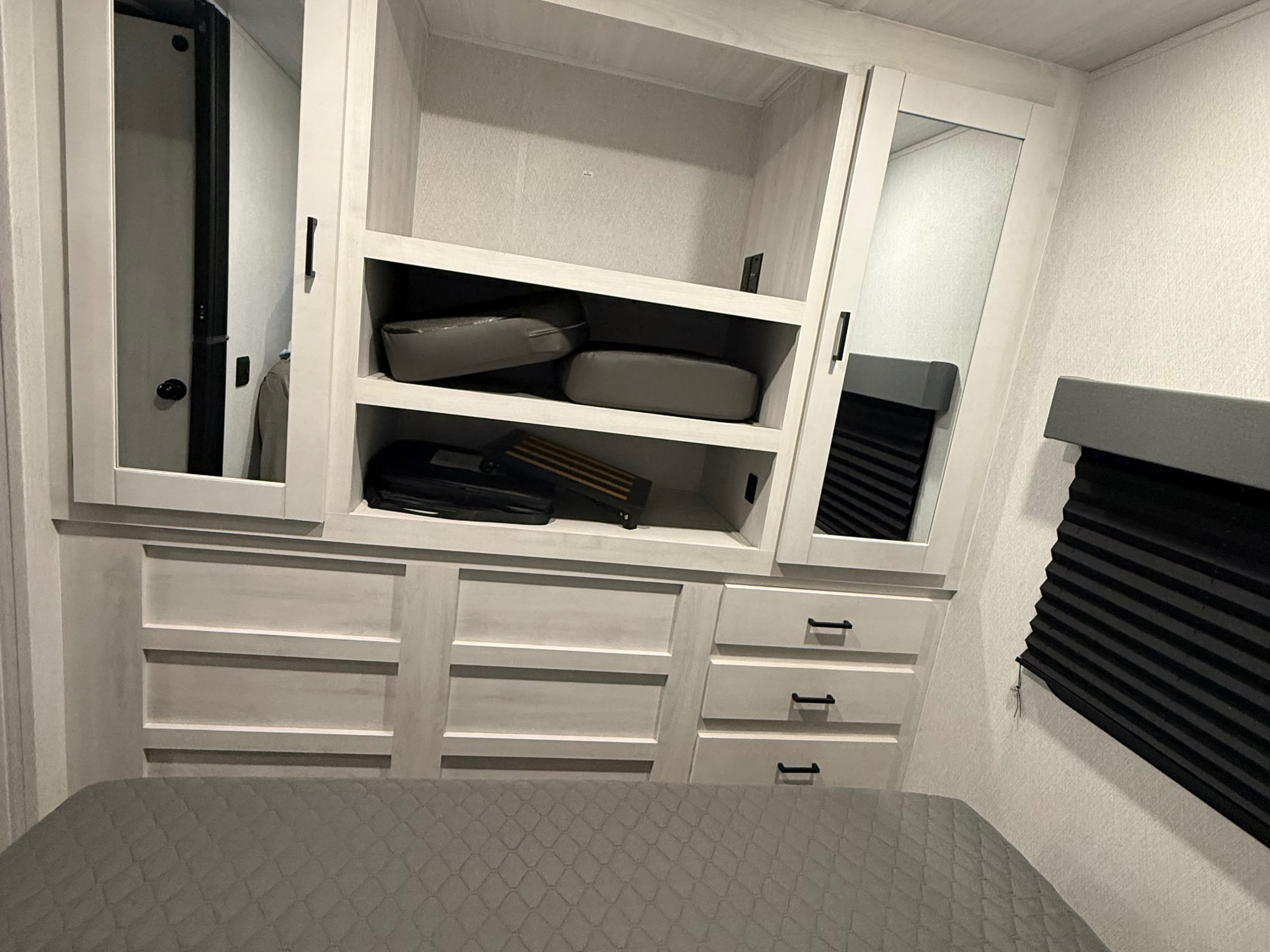 RV rental bedroom: Gray bed, light built-in cabinets with mirrors, shelves, drawers, and an overhead AC unit.. East to West Entrada 2025
