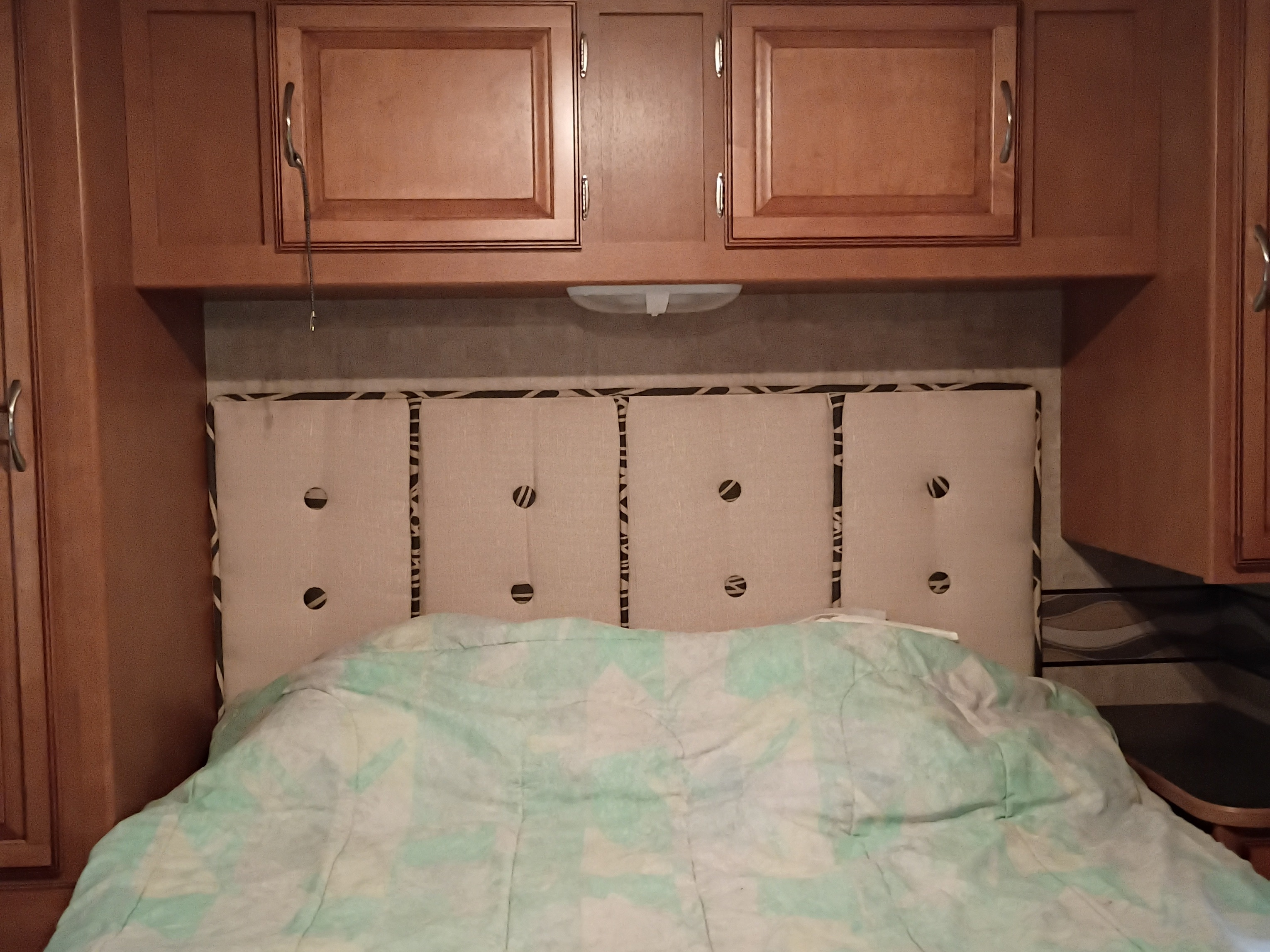 Cozy RV rental bedroom featuring overhead wooden cabinets, a tufted headboard, and a light green patterned blanket.. Winnebago Minnie Winnie 2016