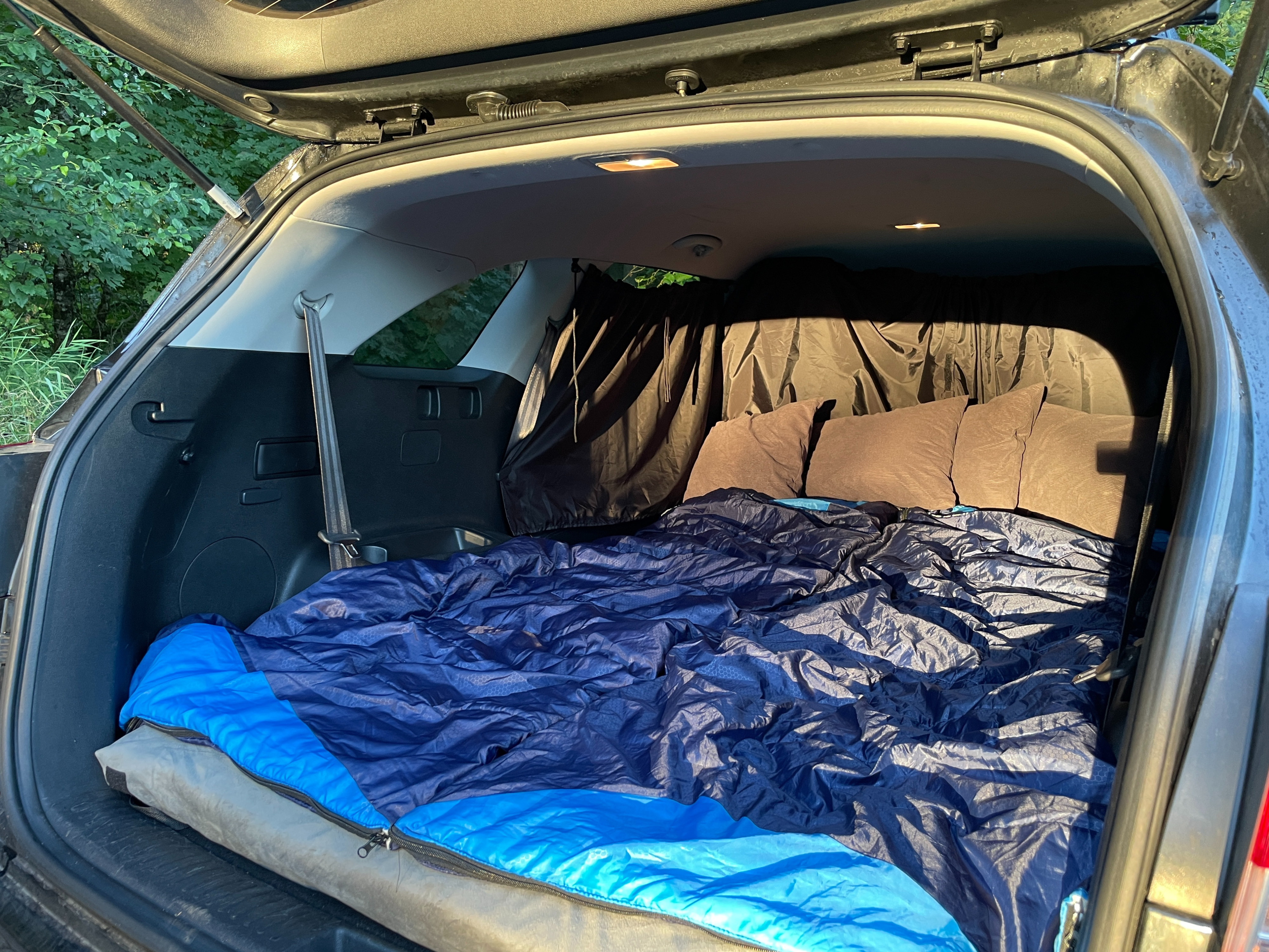 Cozy car camping setup in an SUV, featuring a sleeping bag, pillows, and privacy curtains. A great alternative to an rv rental.. KIA Sorento 4X4 2017