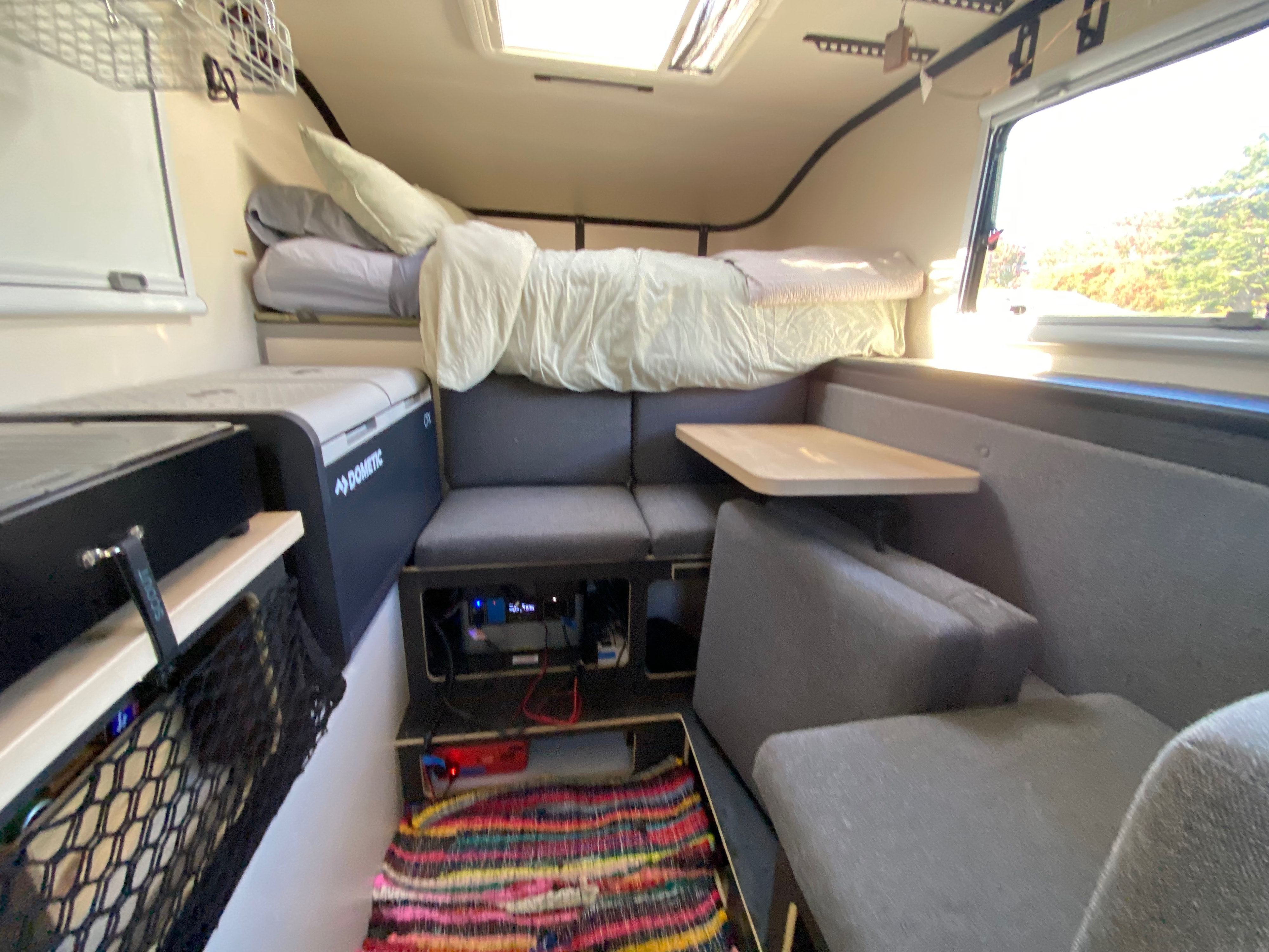 Cozy rv rental interior with an overhead bed, Dometic fridge, dinette, and window showcasing a bright outdoor view.. Mobile Scout Dodge Ram 2500 2021