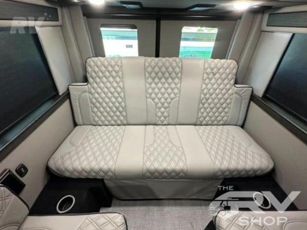 Inside this luxurious rv rental, a light-colored quilted bench seat converts to a bed, flanked by windows and additional seating.. Midwest Automotive Designs Passage 2024
